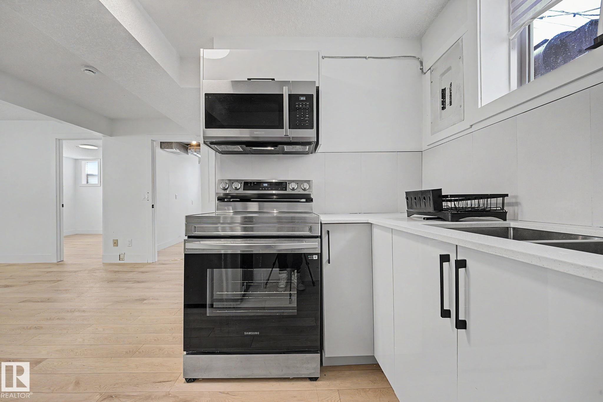 Contemporary kitchen featuring white cabinetry, a stainless steel electric range, an over-range microwave, and a double basin sink - 11914 124 Street, Edmonton, AB