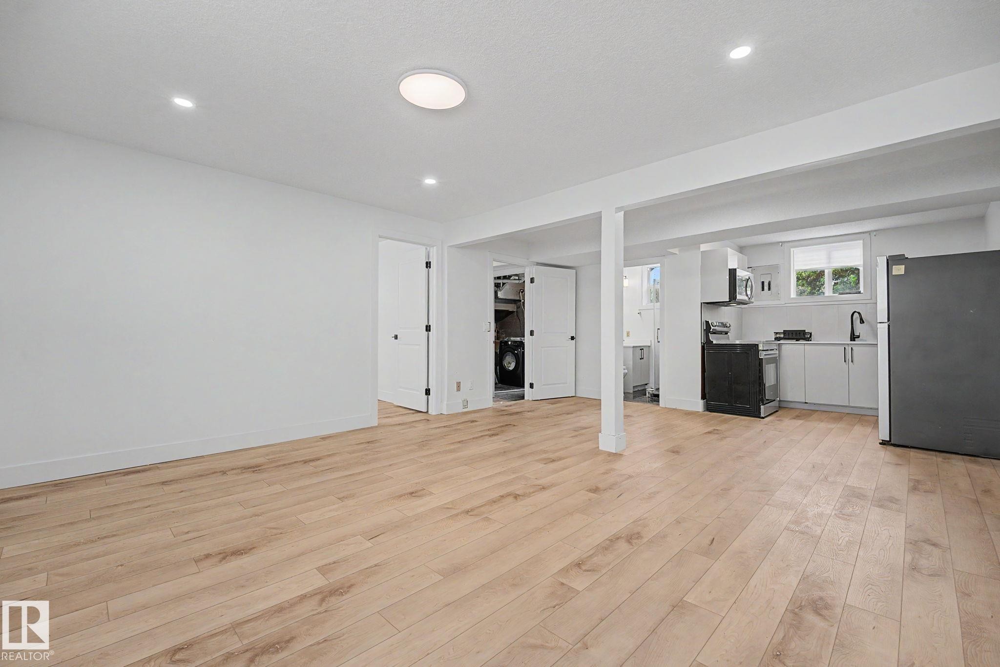 Open-concept living area featuring light wood-finish flooring, recessed lighting, and a modern kitchen with white cabinetry - 11914 124 Street, Edmonton, AB