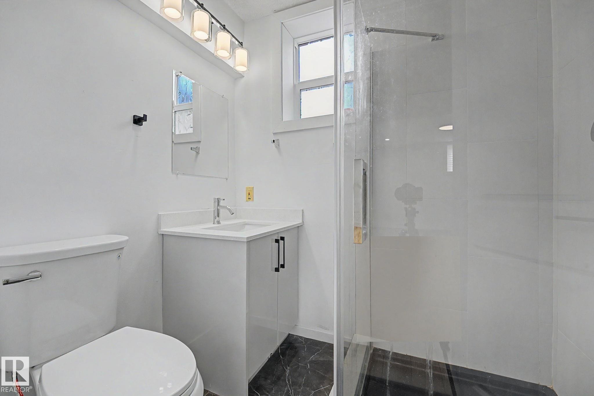 Bathroom featuring a glass-enclosed shower, a white vanity with a single sink, and a modern light fixture - 11914 124 Street, Edmonton, AB
