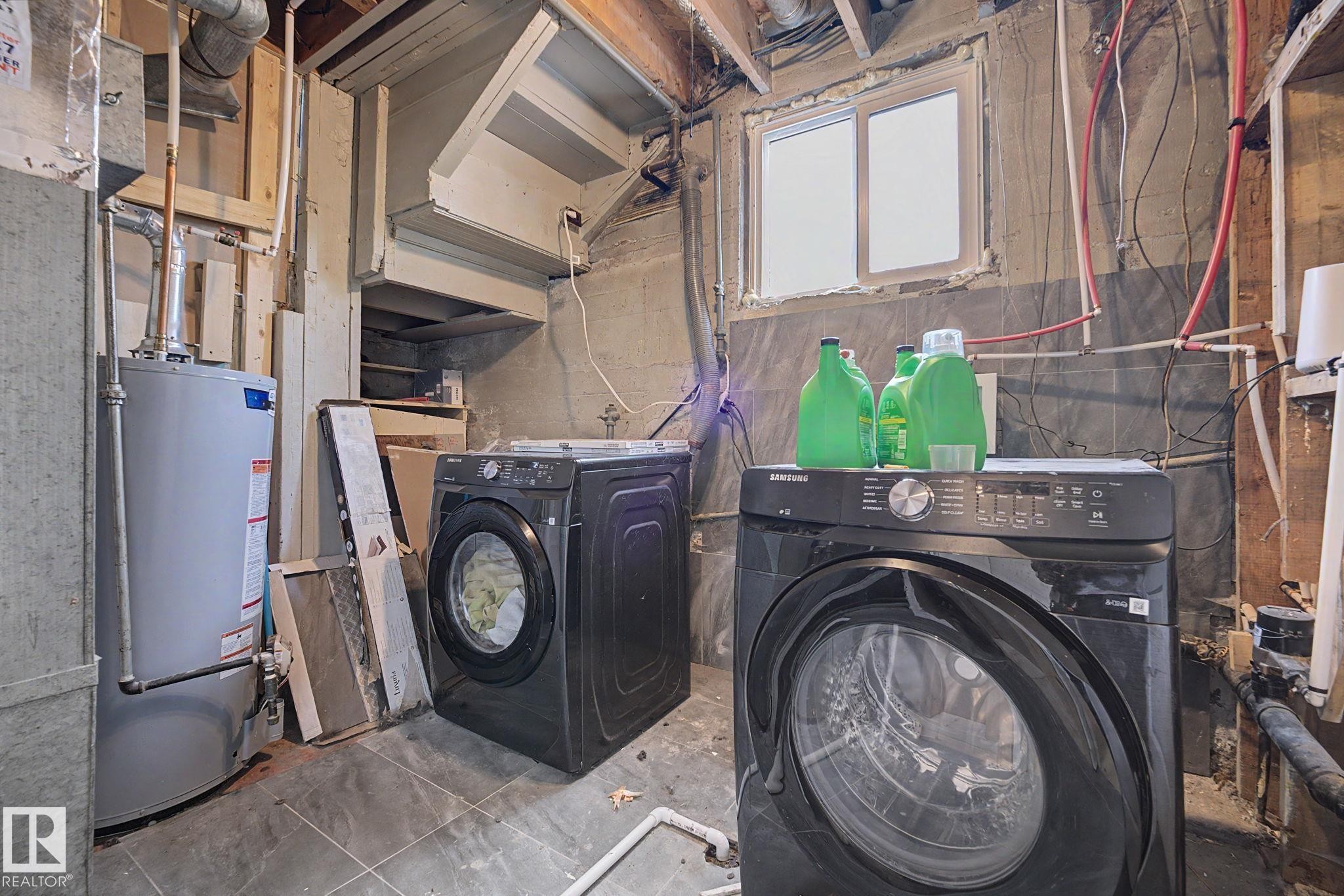 Laundry area featuring a window, visible utility piping, exposed ceiling joists, and a hot water heater - 11914 124 Street, Edmonton, AB