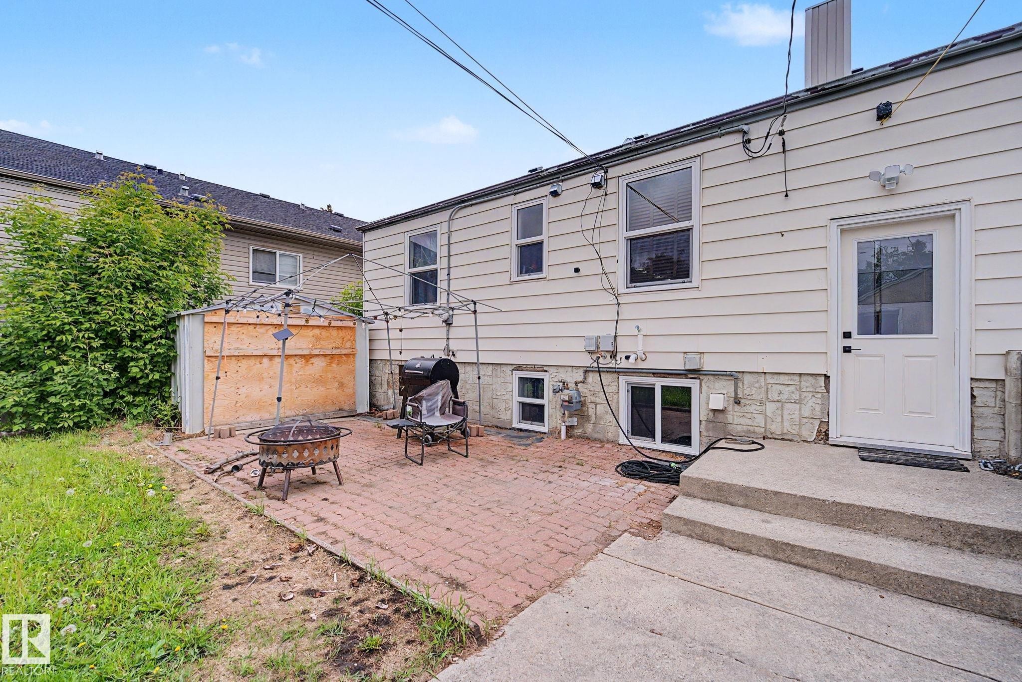 Backyard patio area featuring a brick paver surface, concrete steps, and a white exterior door - 11914 124 Street, Edmonton, AB