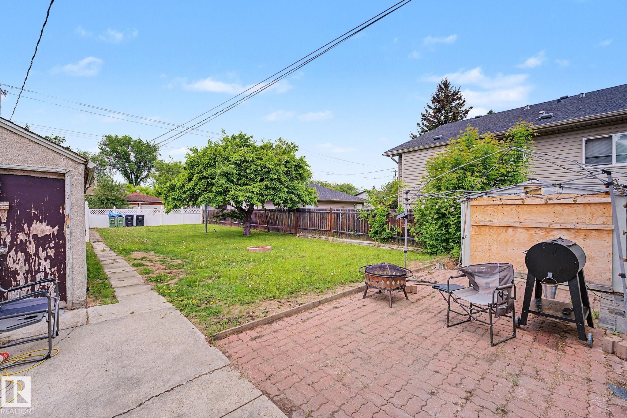 Expansive backyard featuring a mature tree, a paved brick patio, and a grass lawn - 11914 124 Street, Edmonton, AB
