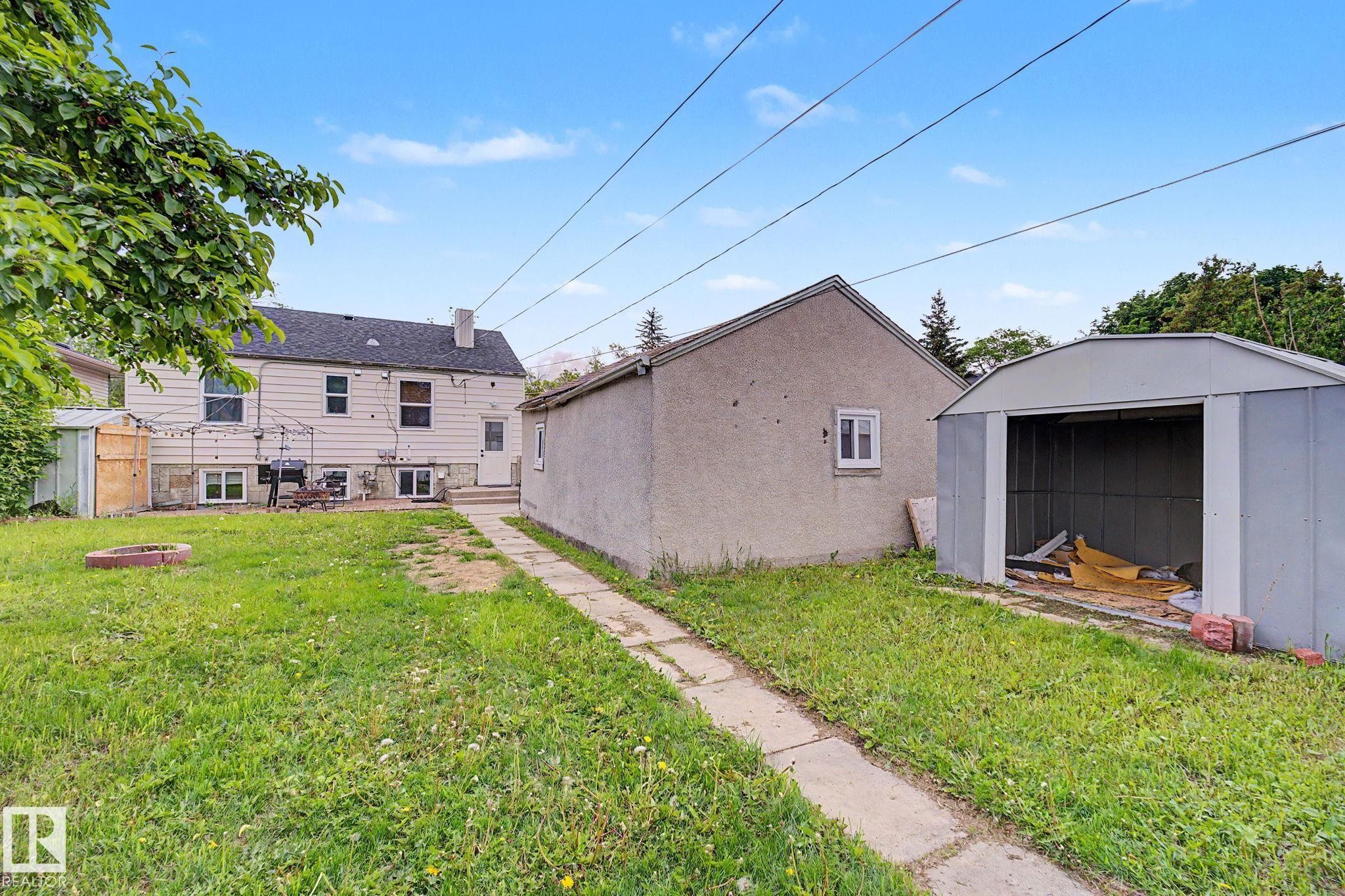 Expansive grassy yard with concrete pathway, detached garage, and metal shed - 11914 124 Street, Edmonton, AB