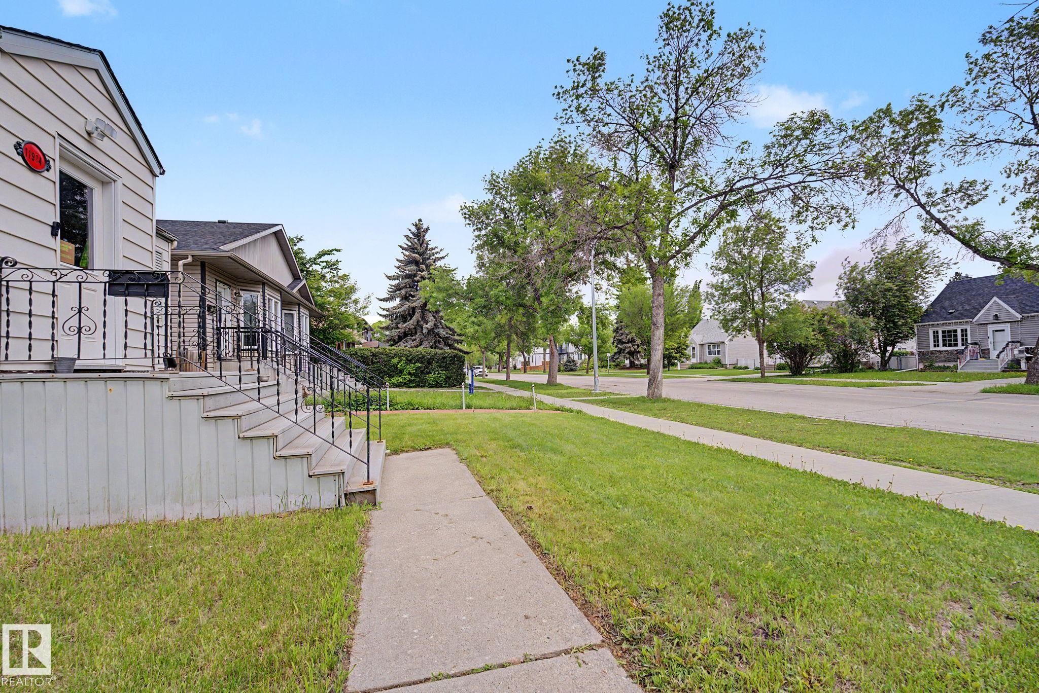 Exterior siding with a raised porch, featuring black wrought iron railings and concrete steps - 11914 124 Street, Edmonton, AB