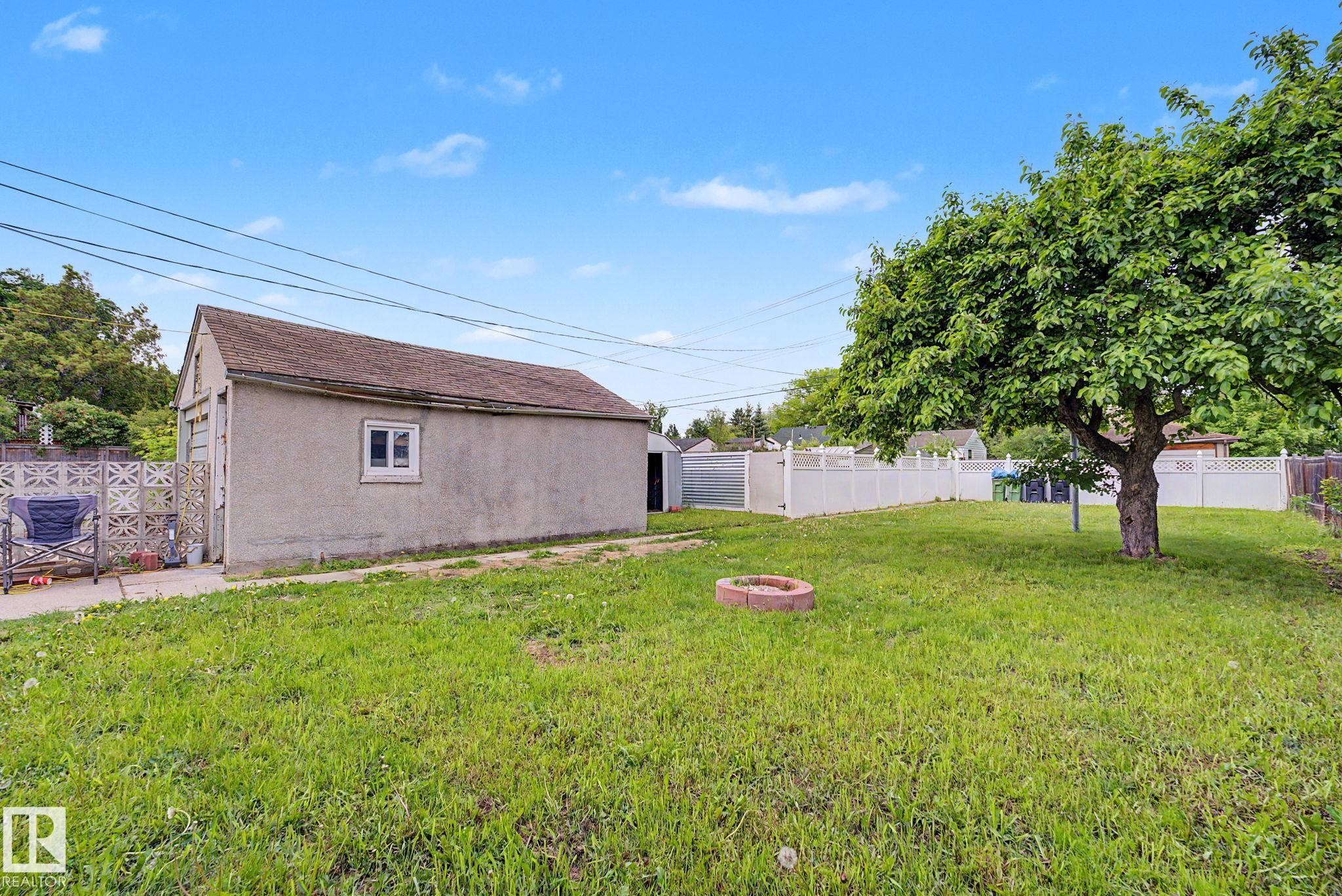 Spacious backyard featuring a stucco detached garage with a single window, a mature tree, and partial white fencing - 11914 124 Street, Edmonton, AB