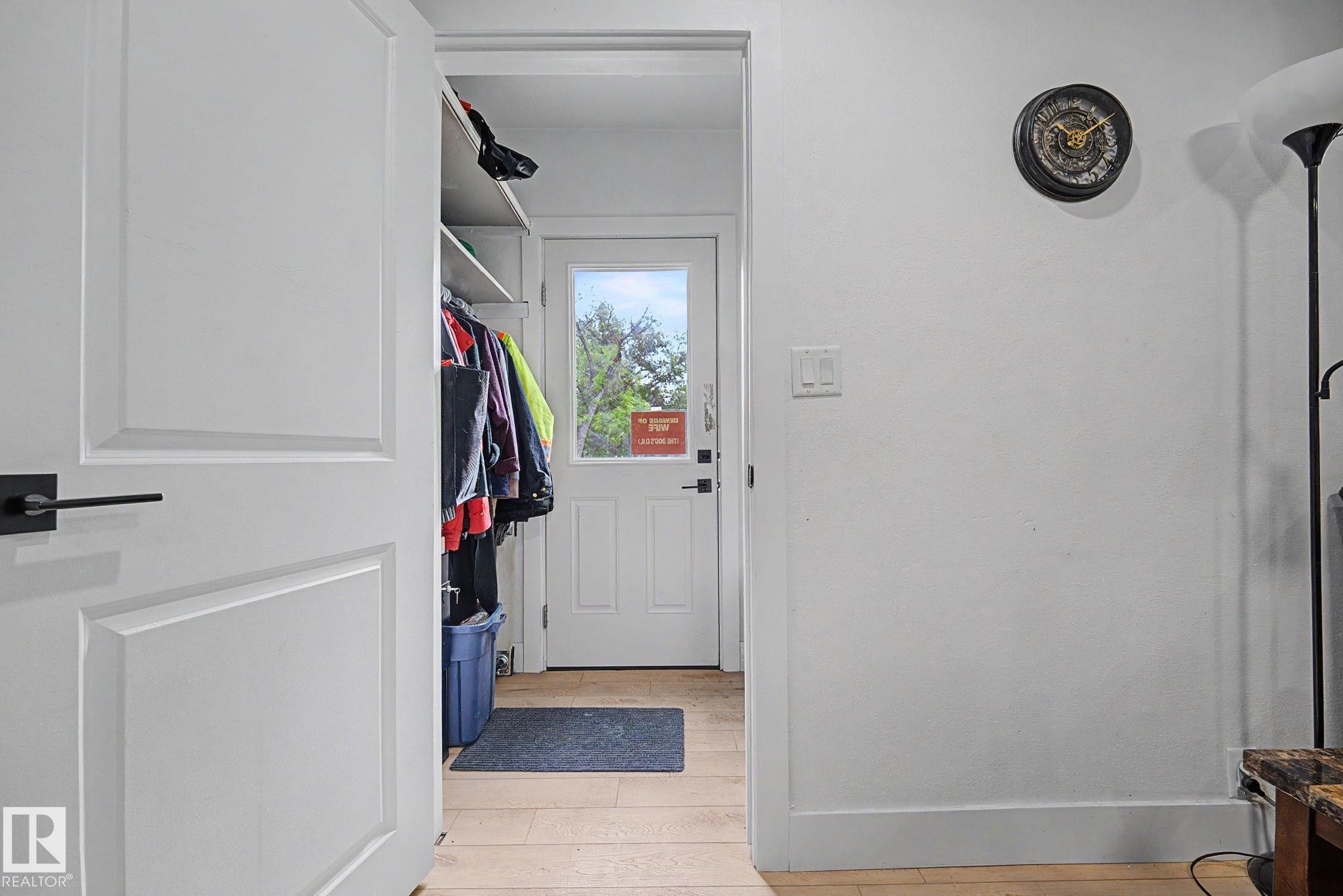 Entryway featuring a white paneled door with matte black hardware, light wood-finish flooring, and white painted walls - 11914 124 Street, Edmonton, AB