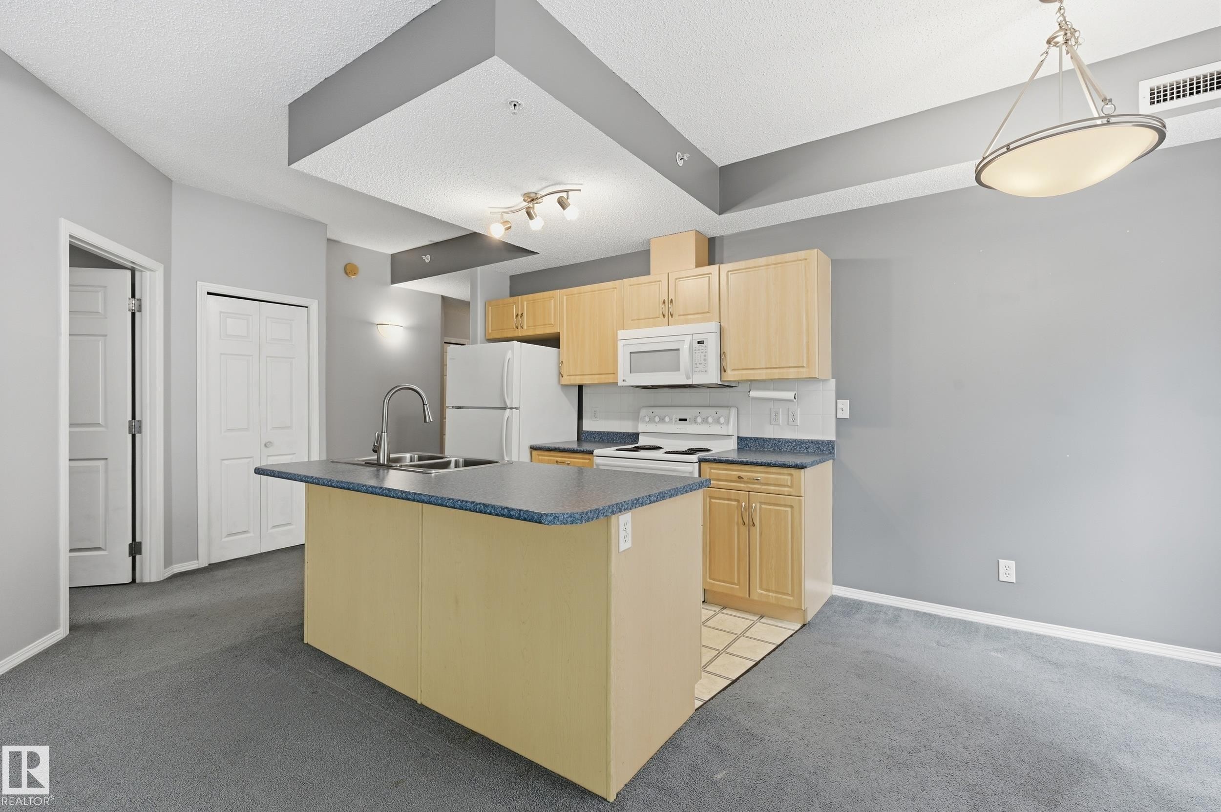 Kitchen featuring light wood-finish cabinetry, white appliances, and a central island with a double basin sink - 203 11103 84 Avenue, Edmonton, AB