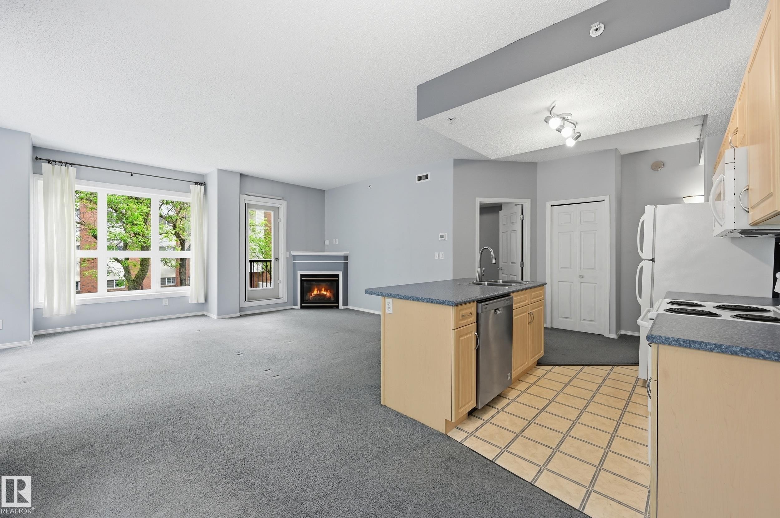 Open-concept living space featuring a gas fireplace with a mantel, a large window, and a door to a balcony - 203 11103 84 Avenue, Edmonton, AB