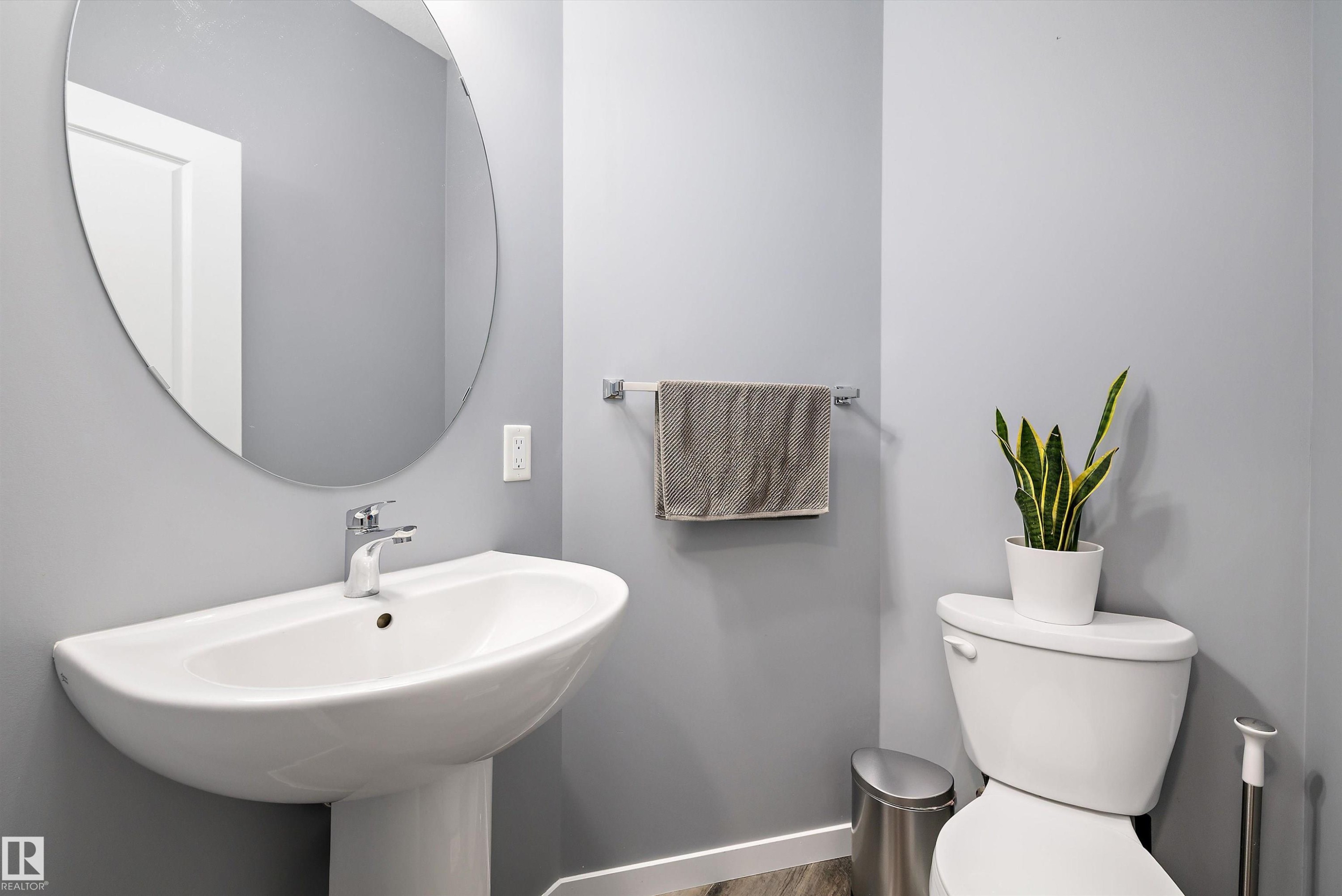 Pedestal sink with chrome fixtures, a circular frameless mirror, and light gray wall paint - 2833 Chokecherry Place, Edmonton, AB