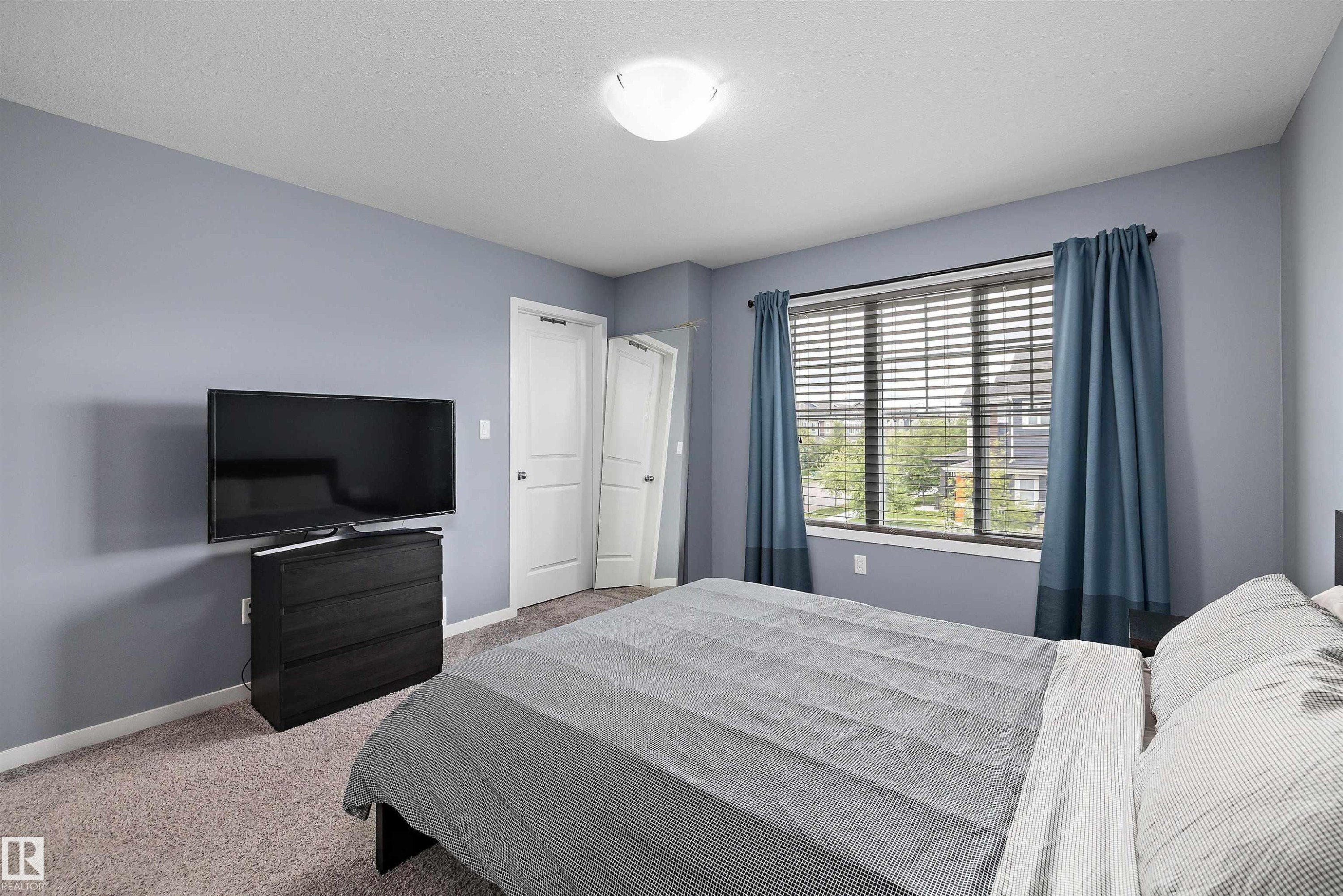 Spacious room featuring light blue walls, two white panel doors, and a large window with horizontal blinds and blue fabric curtains - 2833 Chokecherry Place, Edmonton, AB