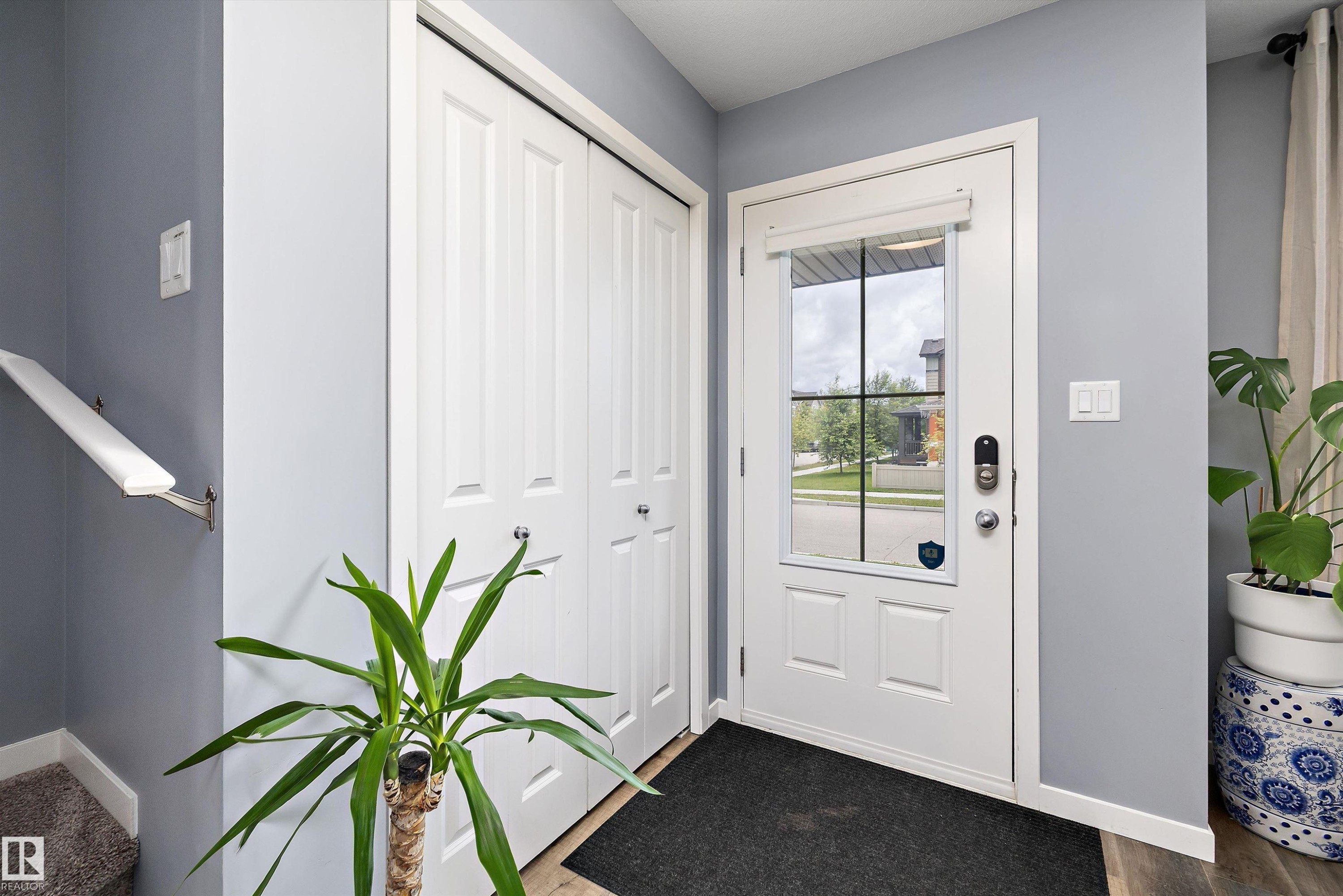 Entryway featuring a paneled door with integrated window, bi-fold closet doors, and wood-finish flooring - 2833 Chokecherry Place, Edmonton, AB