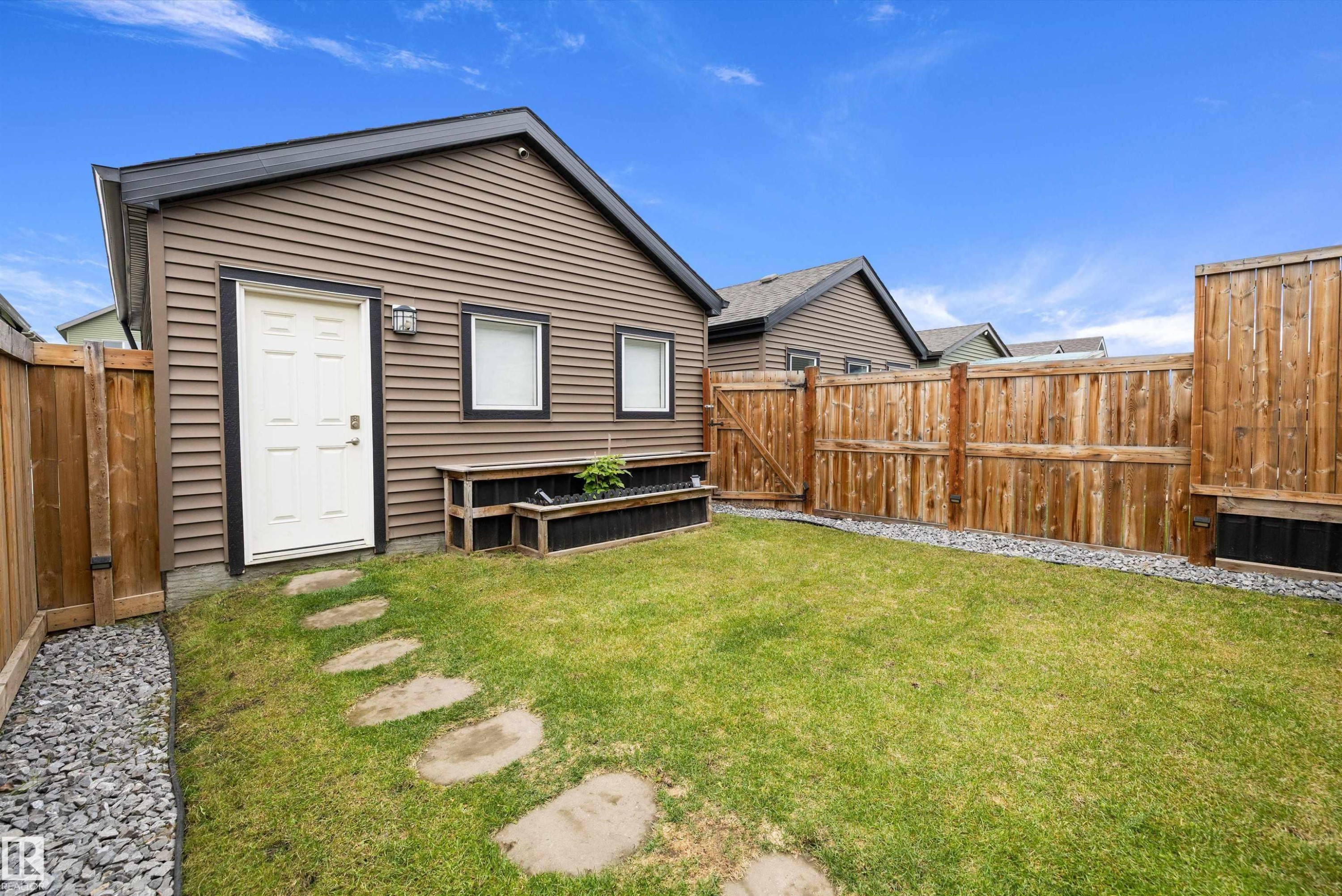 Private yard featuring a manicured lawn, full wood fencing, a stone pathway, and a built-in planter box - 2833 Chokecherry Place, Edmonton, AB