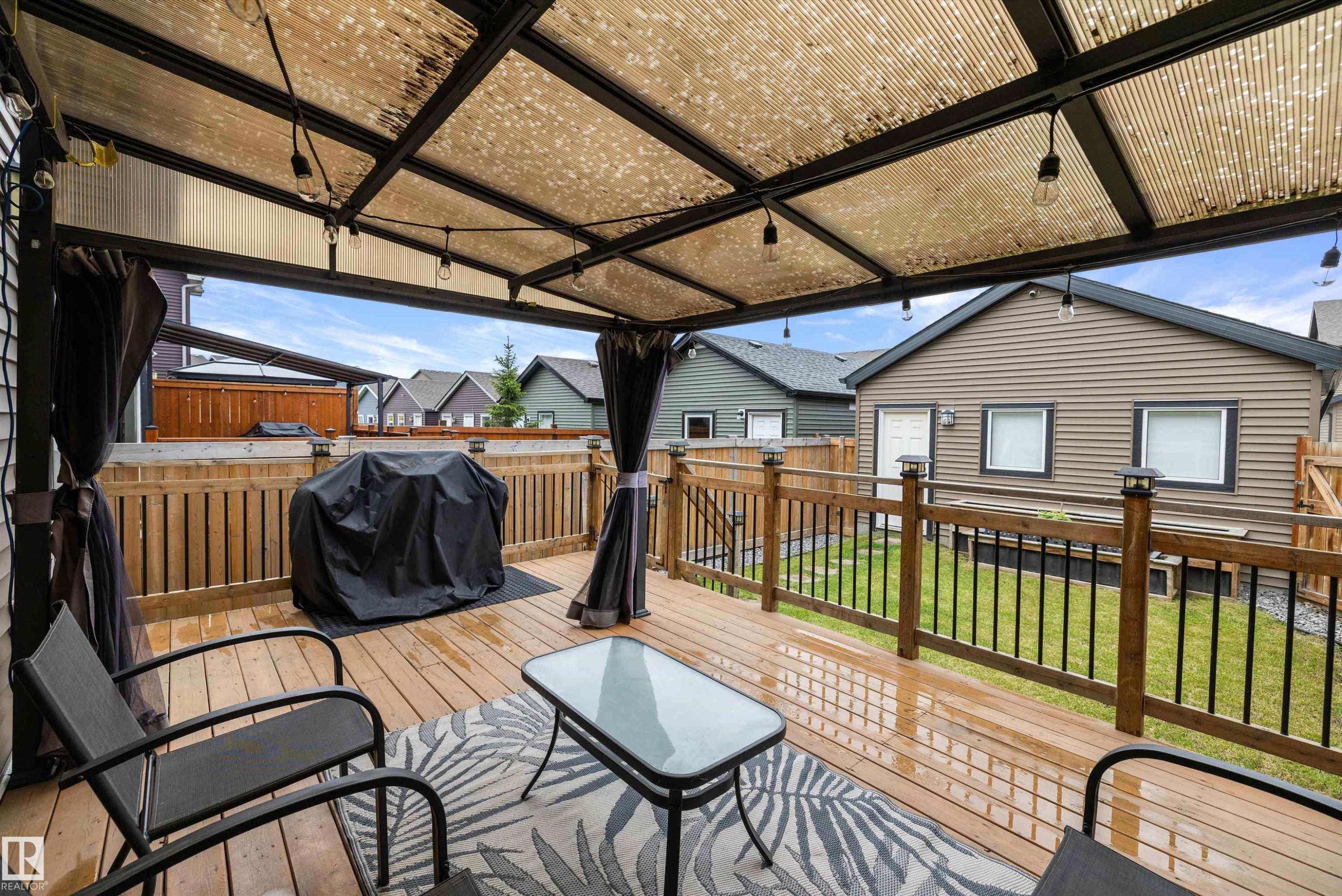 Expansive wood-finish deck featuring a translucent overhead canopy, string lighting, and black privacy curtains - 2833 Chokecherry Place, Edmonton, AB