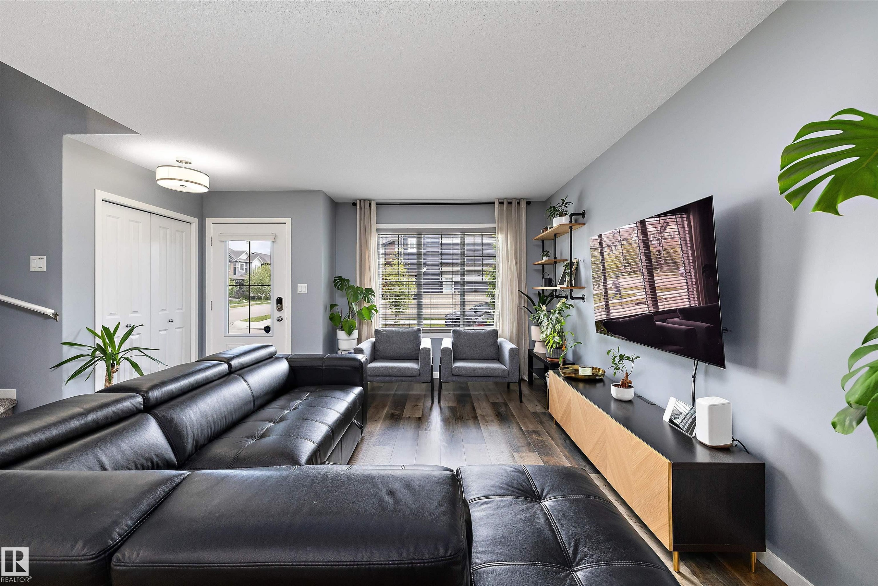 Open-concept living space with wood-finish flooring, a contemporary ceiling light fixture, and a front entry door with integrated window panels - 2833 Chokecherry Place, Edmonton, AB