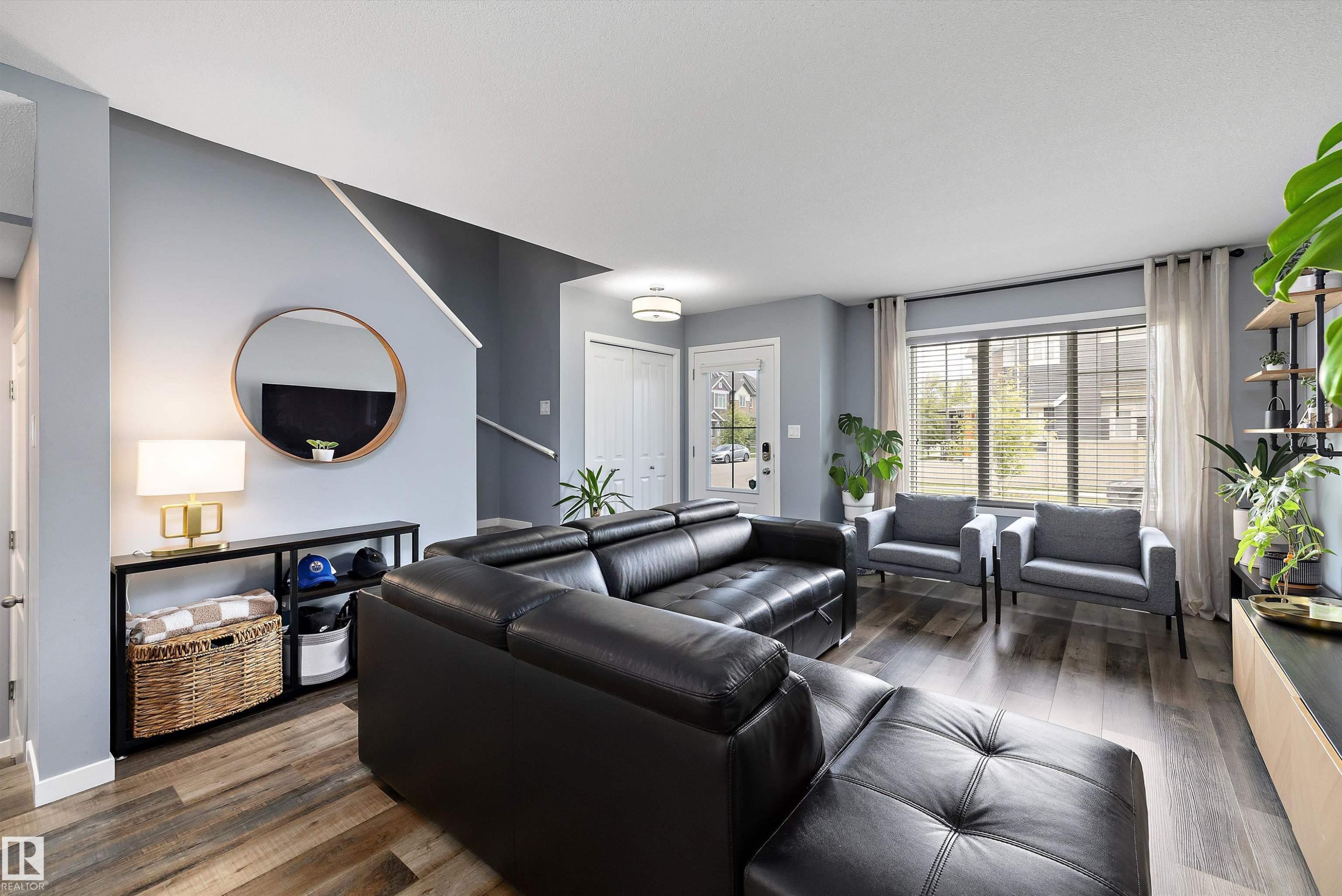 Spacious living area featuring wide-plank wood-finish flooring, a contemporary ceiling light fixture, and a large window with blinds and drapes - 2833 Chokecherry Place, Edmonton, AB