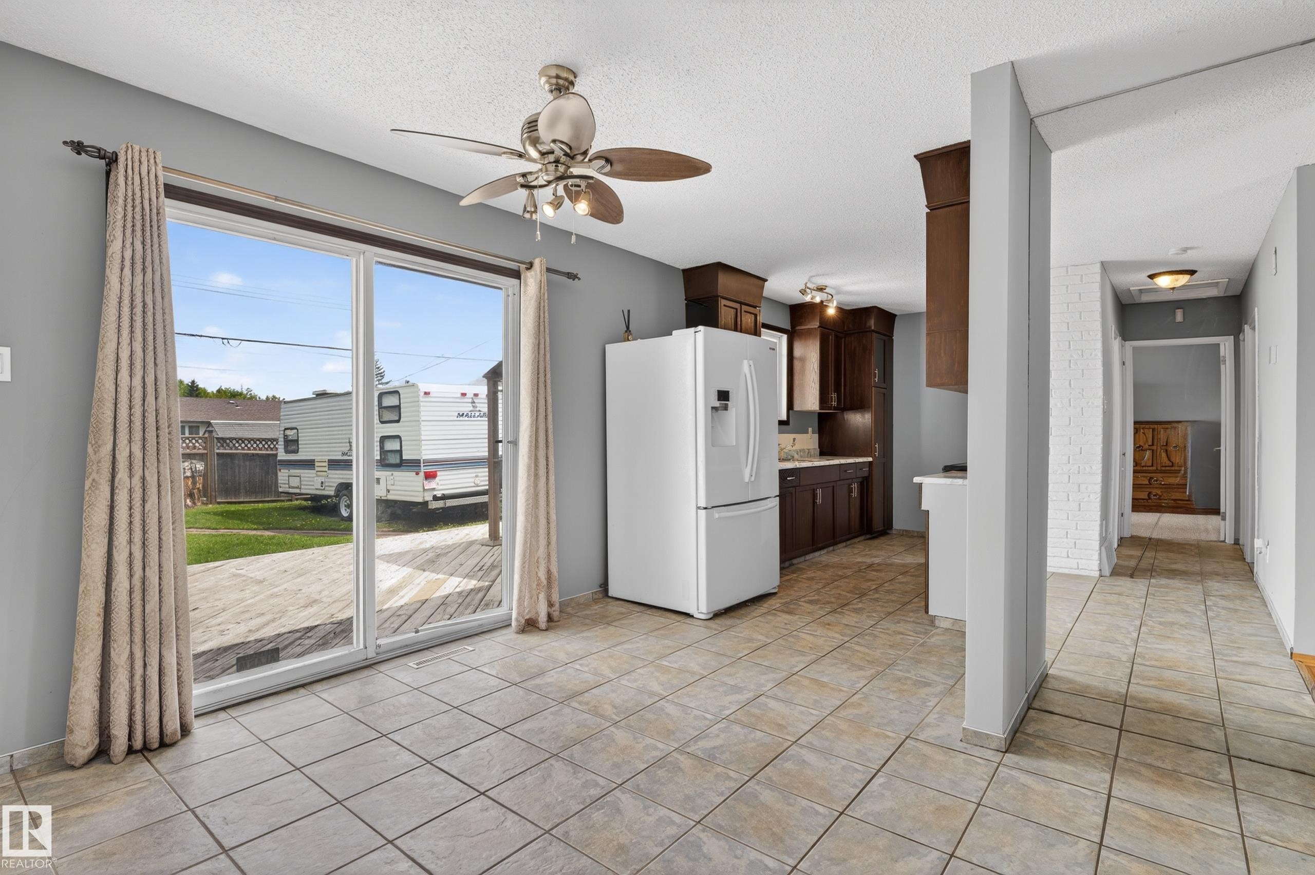 Open-concept living space featuring tile flooring, a ceiling fan, and sliding glass doors leading to a wood-finish deck - 13427 114 Street Nw, Edmonton, AB