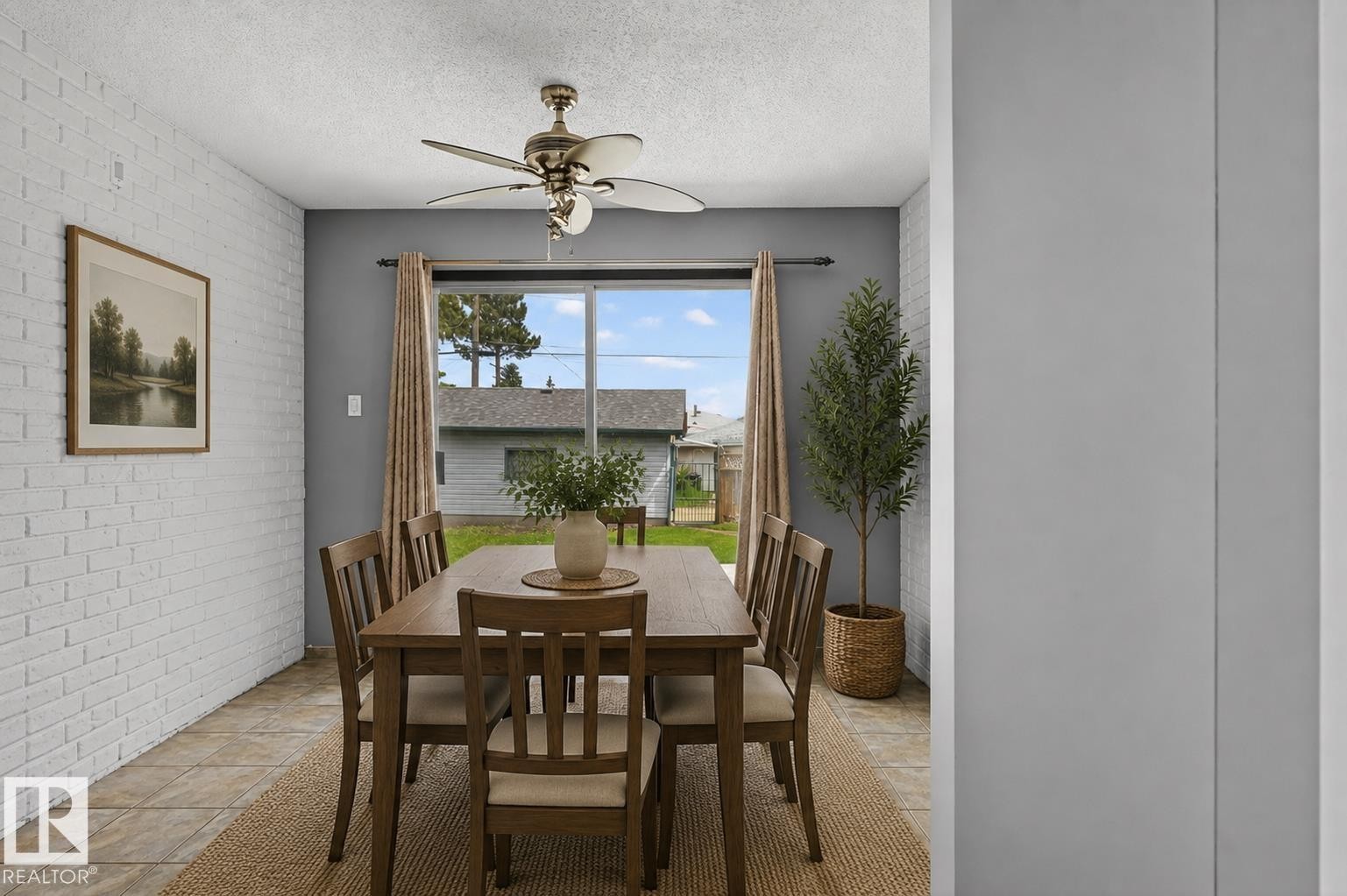 Dining area featuring a sliding glass door, white painted brick accent wall, tiled flooring, ceiling fan, and a neutral color palette - 13427 114 Street Nw, Edmonton, AB