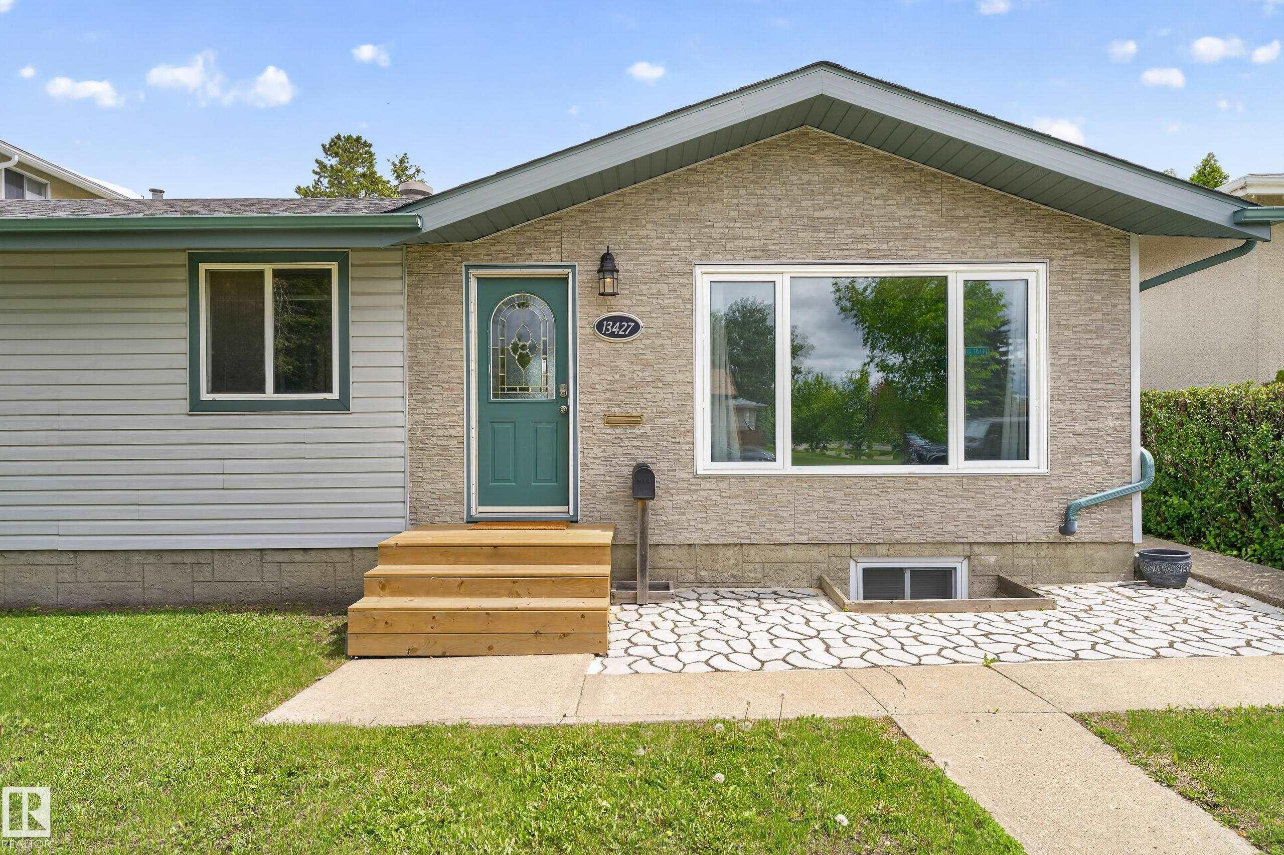 Exterior featuring a teal entry door with decorative glass, new wood steps, a large picture window, and textured stone-look siding - 13427 114 Street Nw, Edmonton, AB