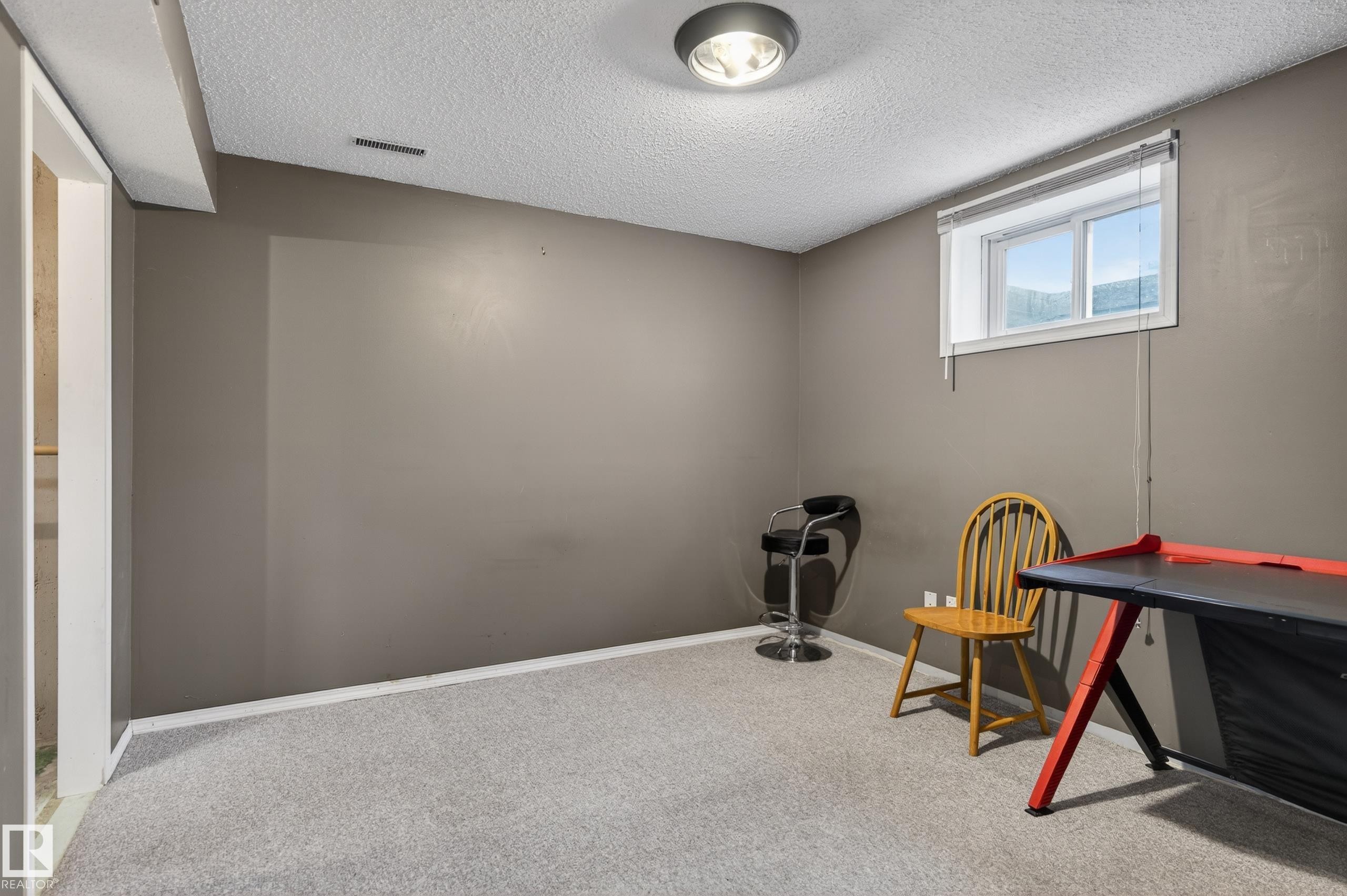 Carpeted room featuring a window with exterior visibility, a ceiling-mounted light fixture, white trim, and neutral wall paint - 13427 114 Street Nw, Edmonton, AB