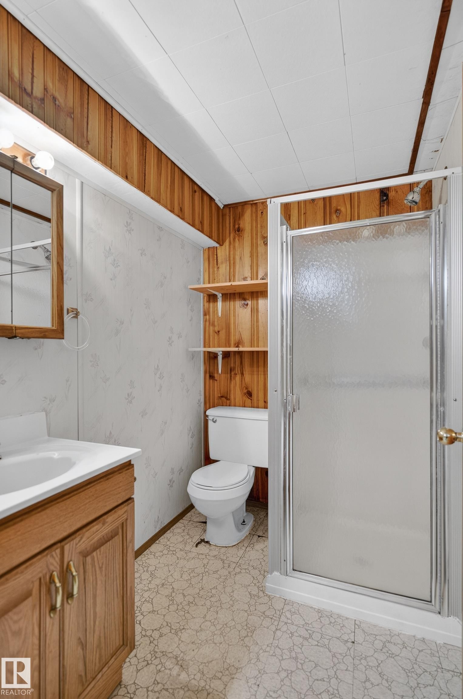 Bathroom featuring a clear glass shower enclosure, wood-finish vanity with an integrated sink, and patterned flooring - 13427 114 Street Nw, Edmonton, AB