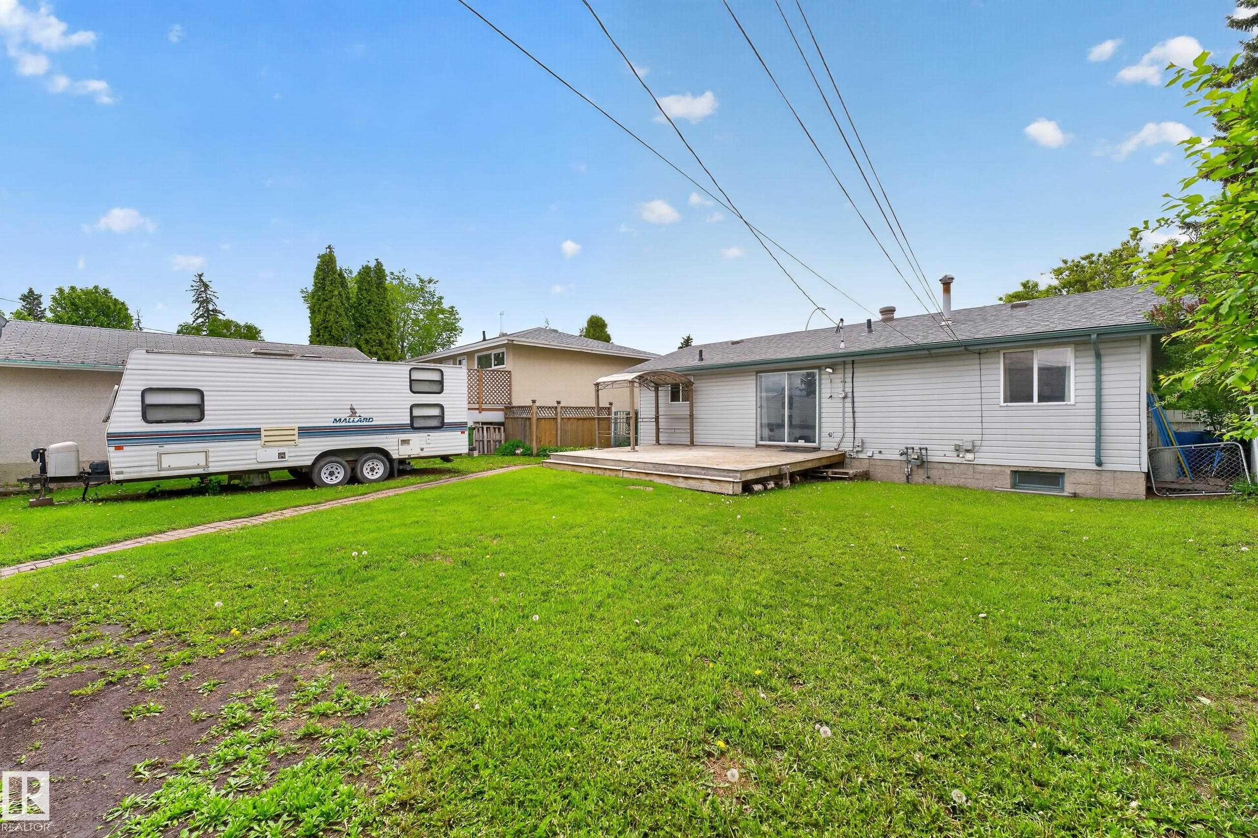 Expansive backyard featuring a large grass area, wood deck, and a sliding glass door entry to the home - 13427 114 Street Nw, Edmonton, AB
