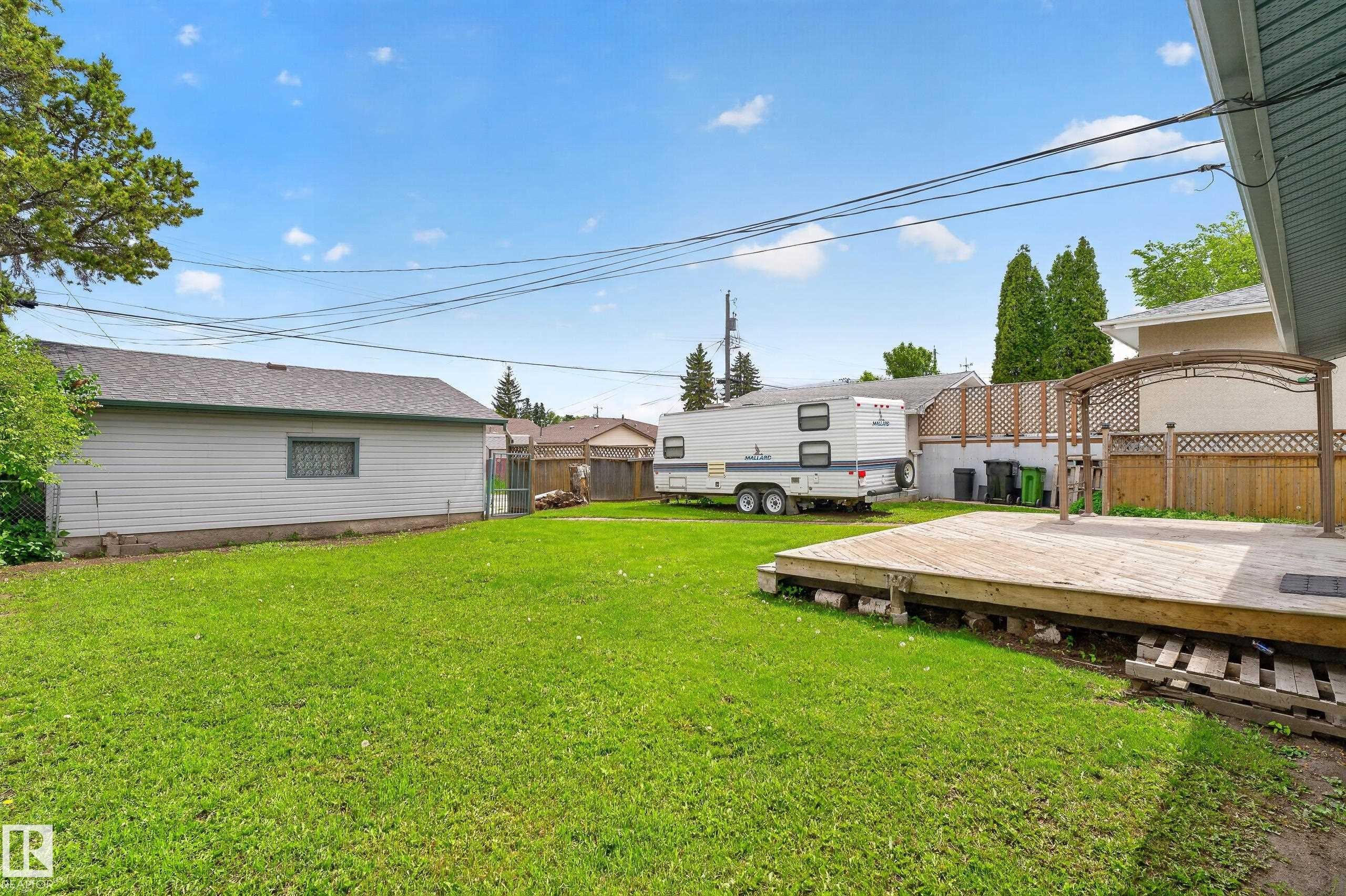 Expansive backyard with a large grass area and a wood deck featuring a decorative pergola structure - 13427 114 Street Nw, Edmonton, AB