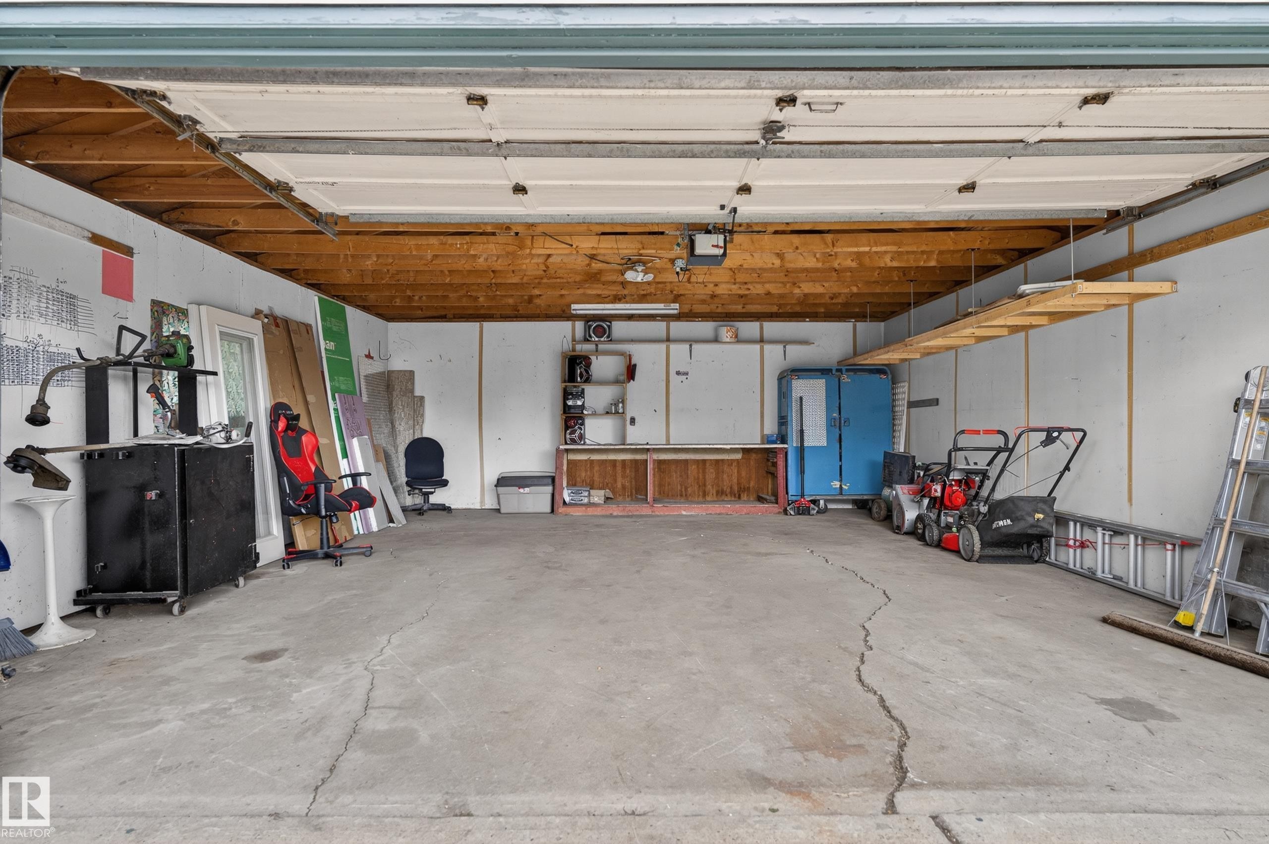Spacious garage with exposed wood ceiling beams, concrete flooring, and ample storage shelving - 13427 114 Street Nw, Edmonton, AB