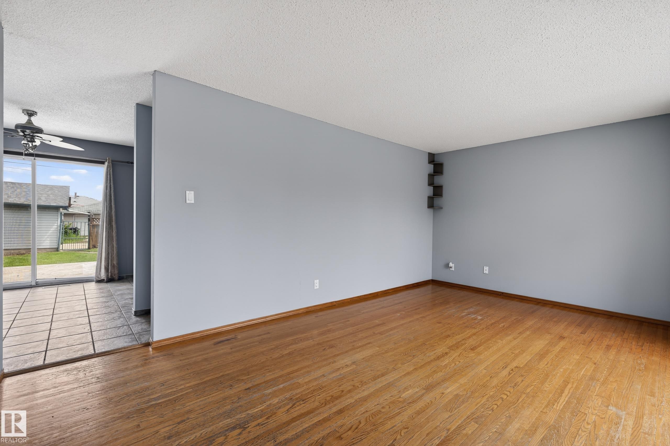 Spacious room with wood-finish flooring, light gray walls, and textured ceiling - 13427 114 Street Nw, Edmonton, AB