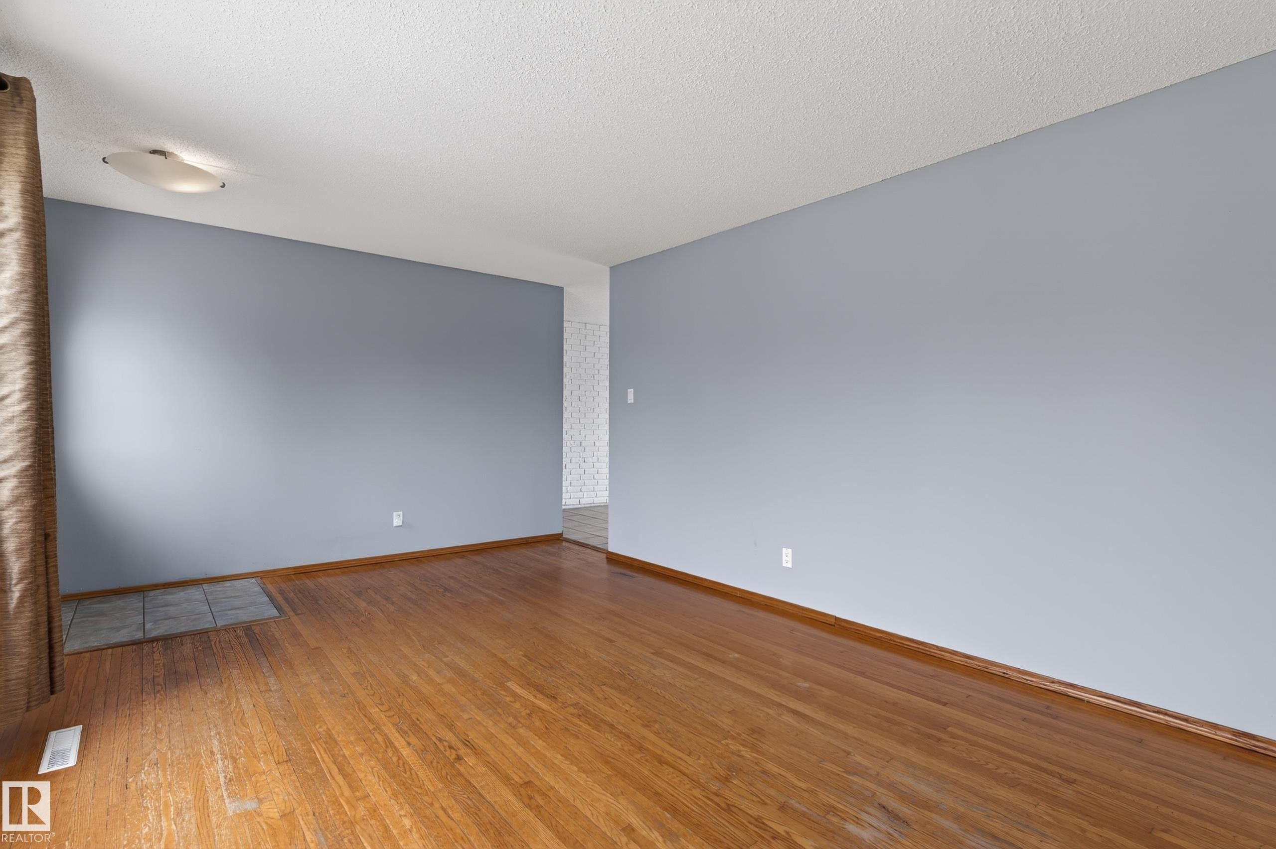 Spacious room featuring wood-finish flooring, light blue painted walls, and white baseboards - 13427 114 Street Nw, Edmonton, AB