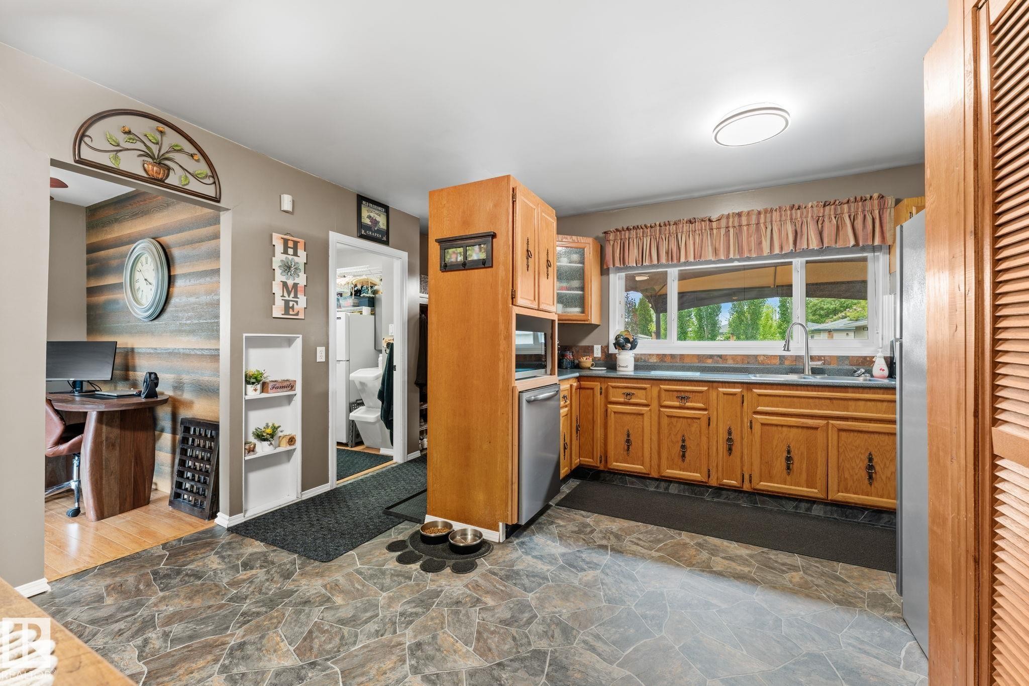 Kitchen featuring wood cabinetry, stainless steel appliances, and a window overlooking exterior landscaping - 11219 134A Avenue, Edmonton, AB