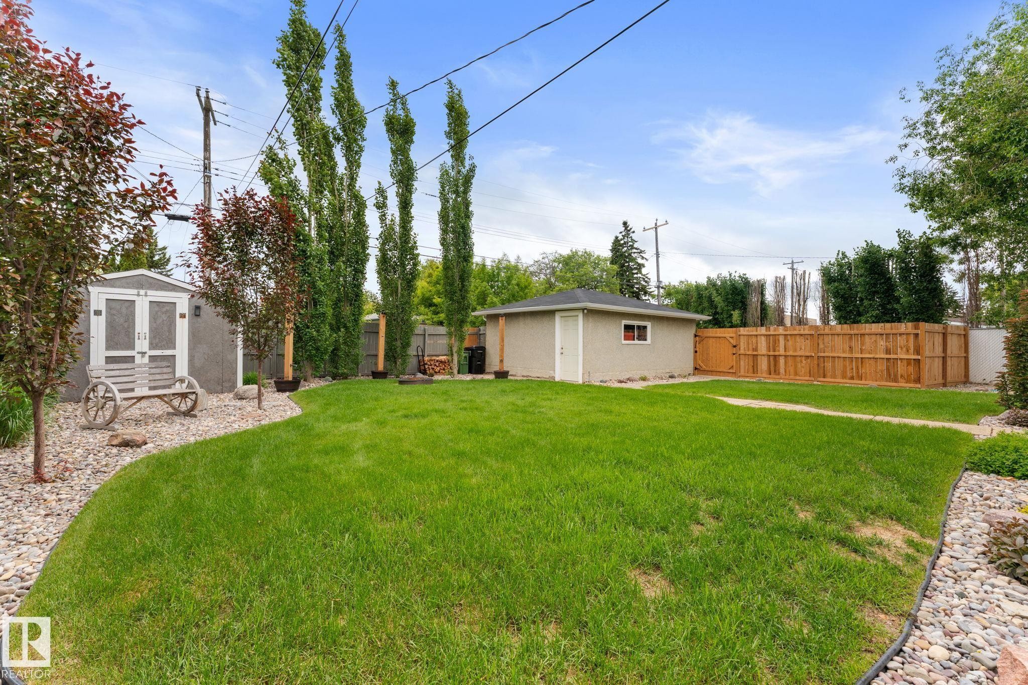 Expansive backyard featuring a manicured lawn, a detached garage, a wood privacy fence, and a storage shed - 11219 134A Avenue, Edmonton, AB