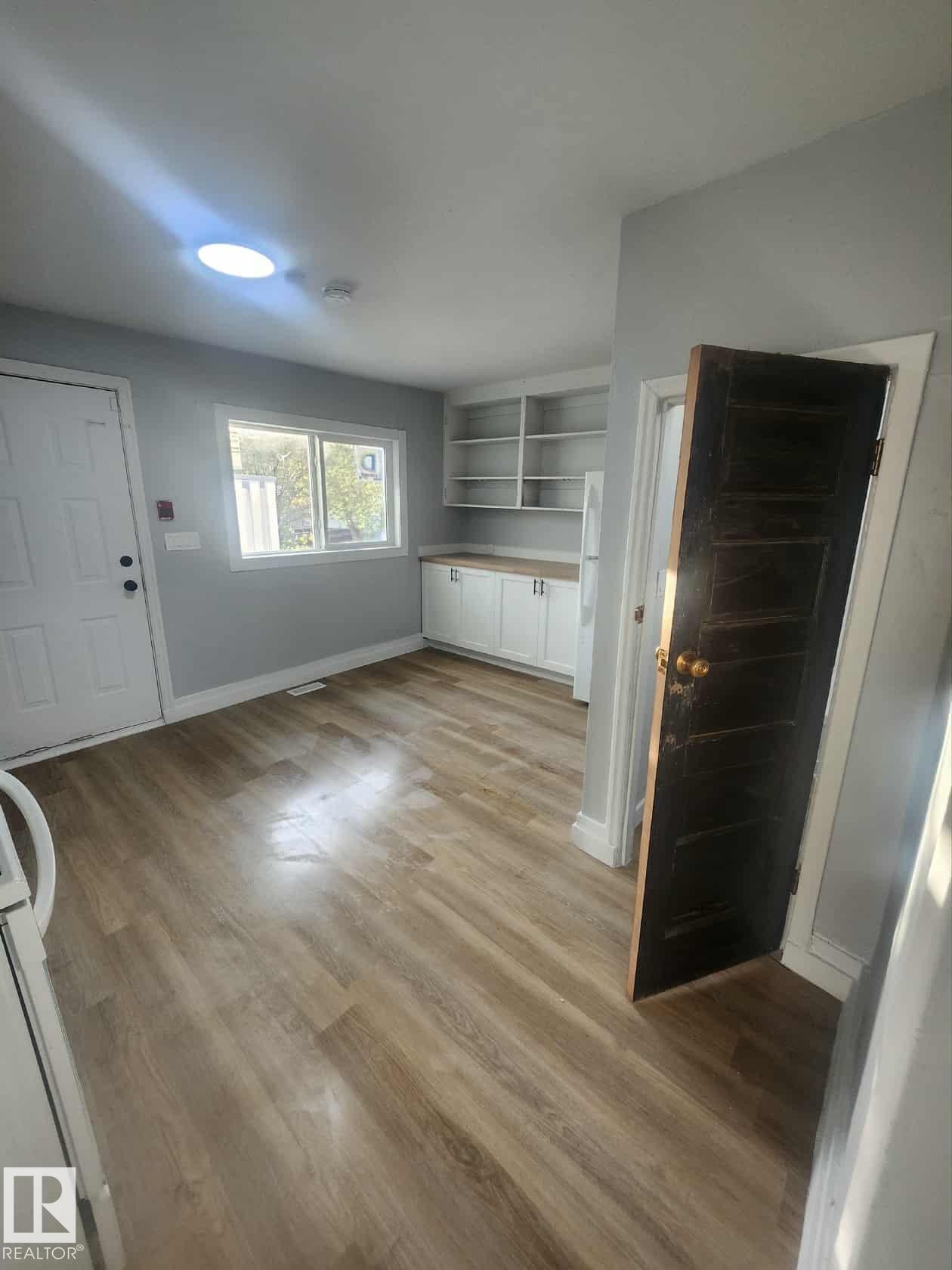 Kitchen area featuring wood-finish flooring, white cabinetry with light countertops, a white exterior door, and a skylight - 11308 94 Street, Edmonton, AB