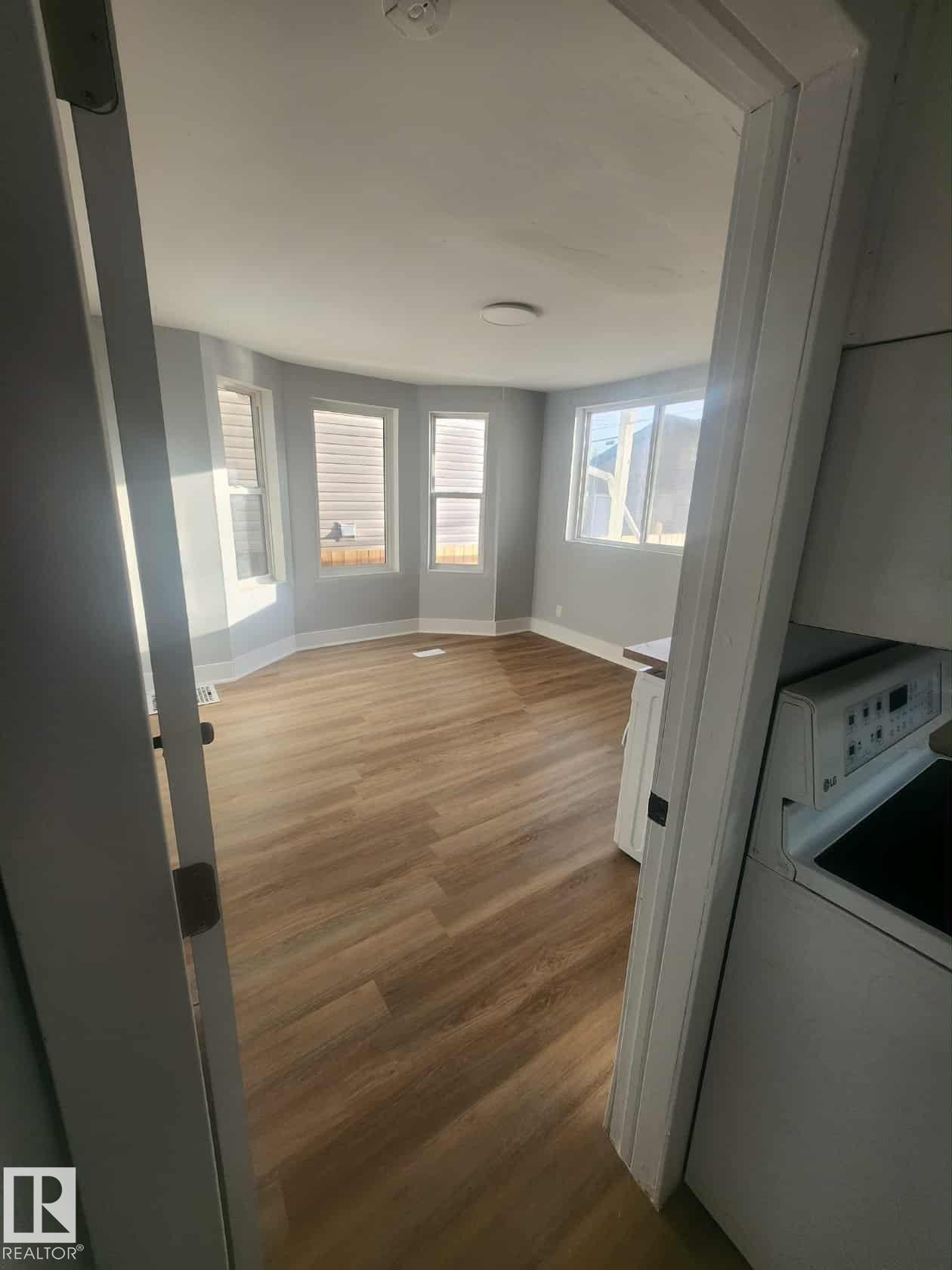 Bright interior space featuring light wood-finish flooring, a bay window with multiple panes, and a flush-mount ceiling light fixture - 11308 94 Street, Edmonton, AB