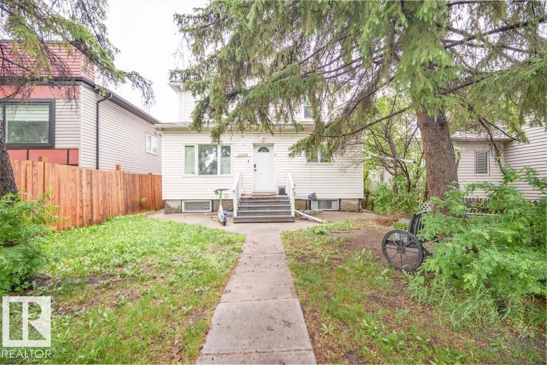 White siding exterior with a prominent front entrance staircase, mature trees, and a concrete walkway - 11308 94 Street, Edmonton, AB