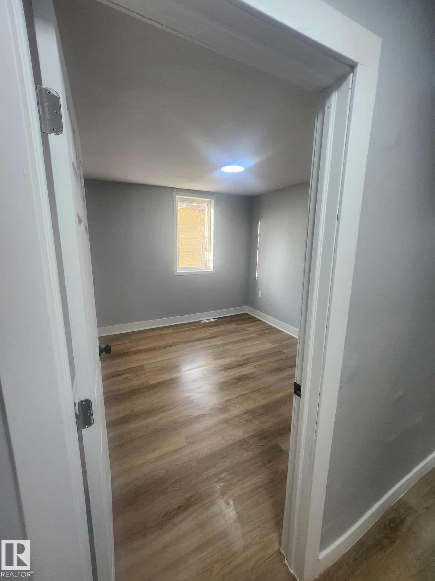 Room featuring wood-finish flooring, light gray walls, a recessed ceiling light, and a window with blinds - 11308 94 Street, Edmonton, AB