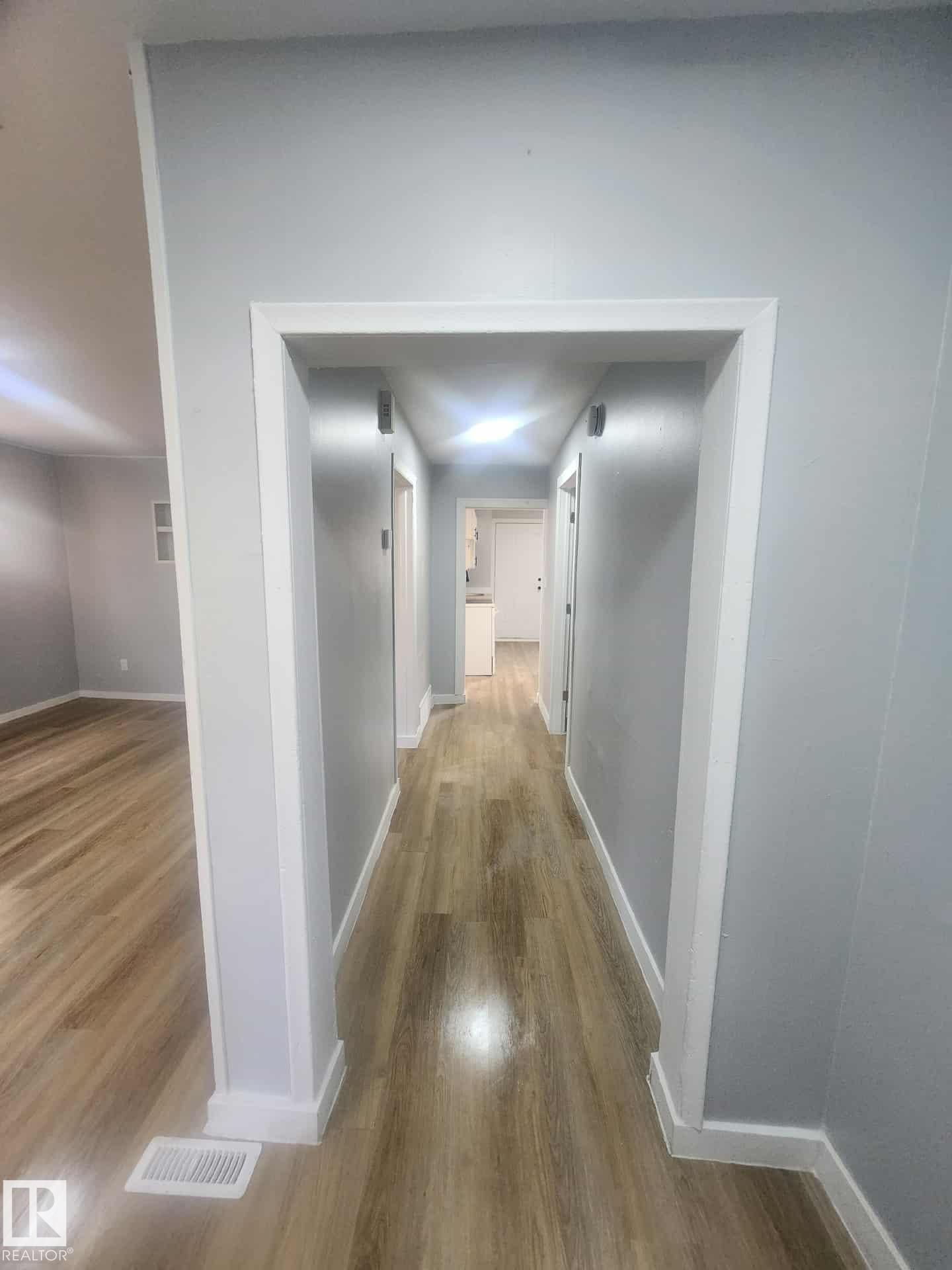 Hallway featuring wood-finish flooring, light grey wall paint, white trim, and recessed lighting - 11308 94 Street, Edmonton, AB