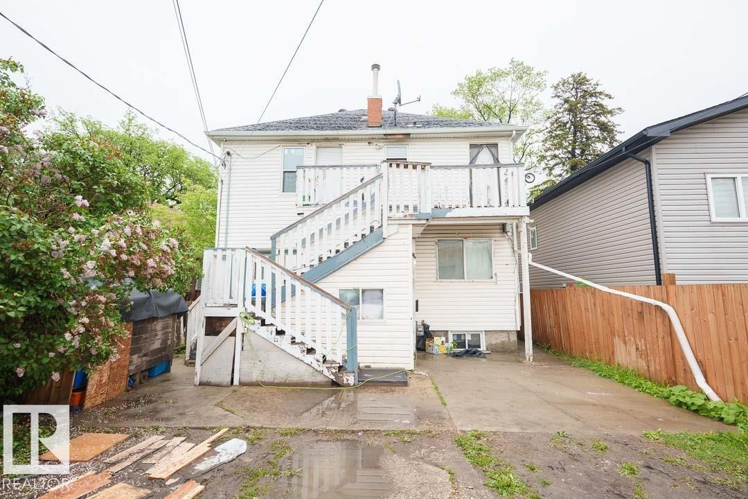 Rear exterior featuring white horizontal siding, a multi-level wooden deck with stairs, a concrete driveway, a wooden fence, and mature foliage - 11308 94 Street, Edmonton, AB