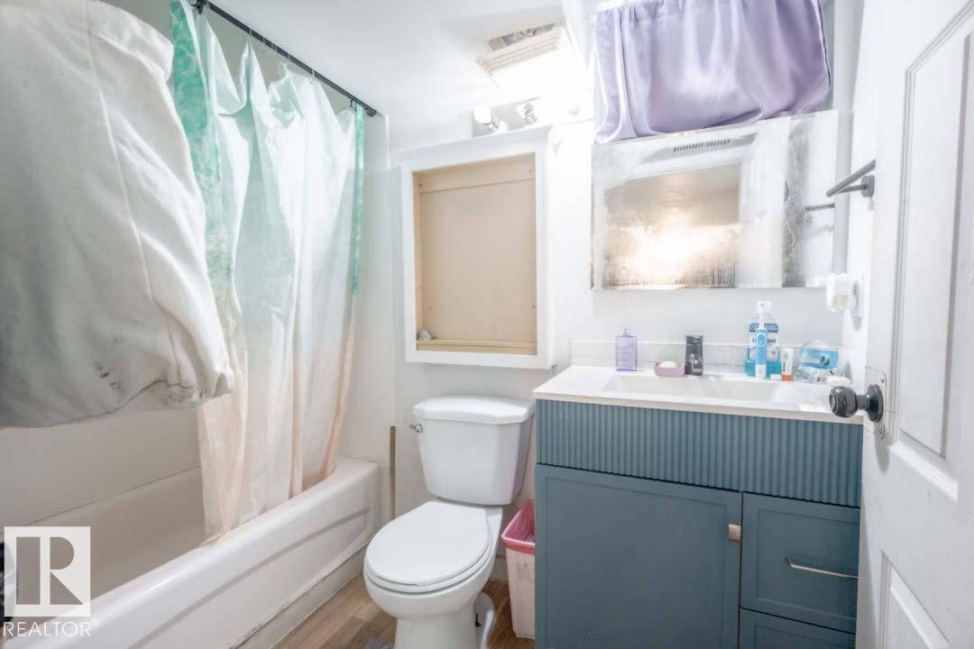 Bathroom featuring a white bathtub with shower, white toilet, and a vanity with a white countertop and blue cabinetry - 11308 94 Street, Edmonton, AB