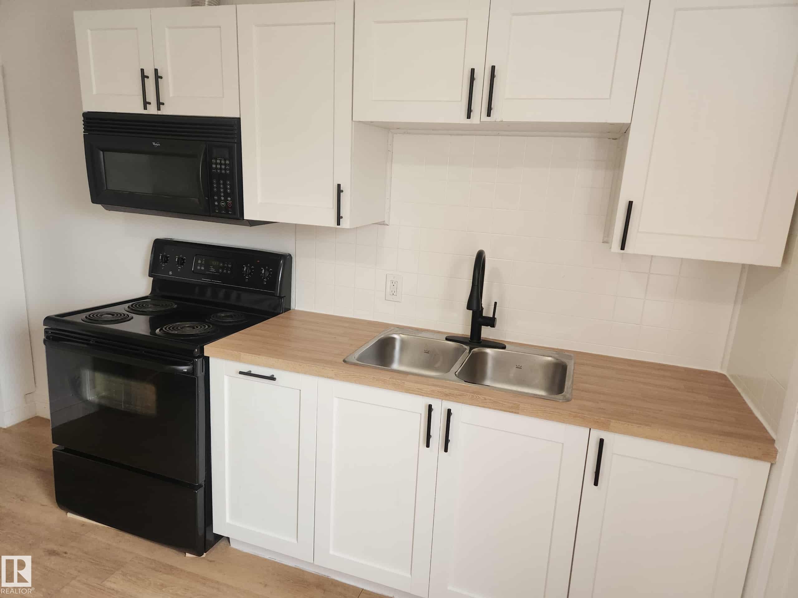 Kitchen featuring white shaker cabinetry with matte black hardware, wood-finish countertops, and a dual stainless-steel sink with a matte black faucet - 11308 94 Street, Edmonton, AB