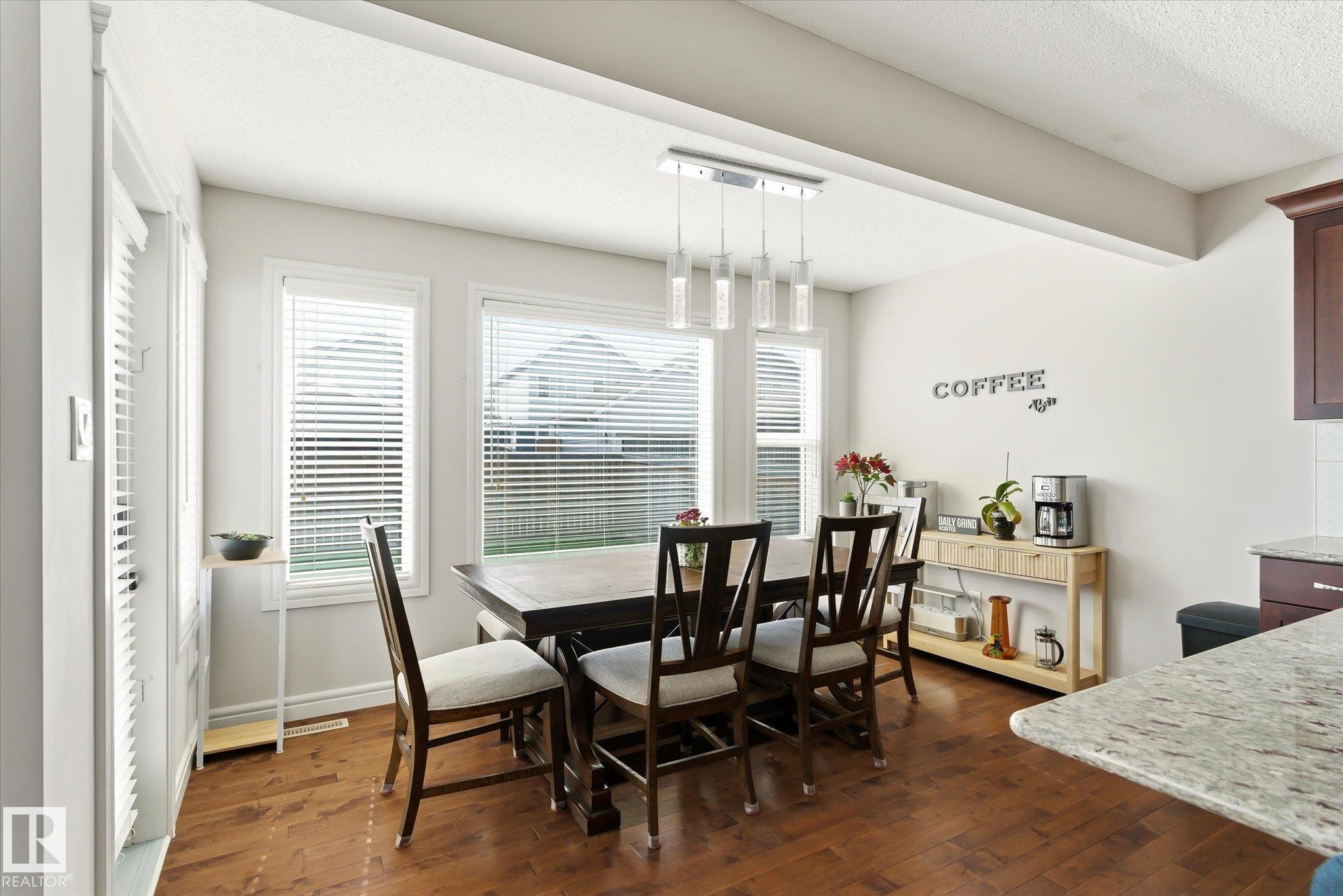 Dining area featuring wood-finish flooring, multiple windows with blinds, and a contemporary linear pendant light fixture - 3685 Westcliff Way, Edmonton, AB