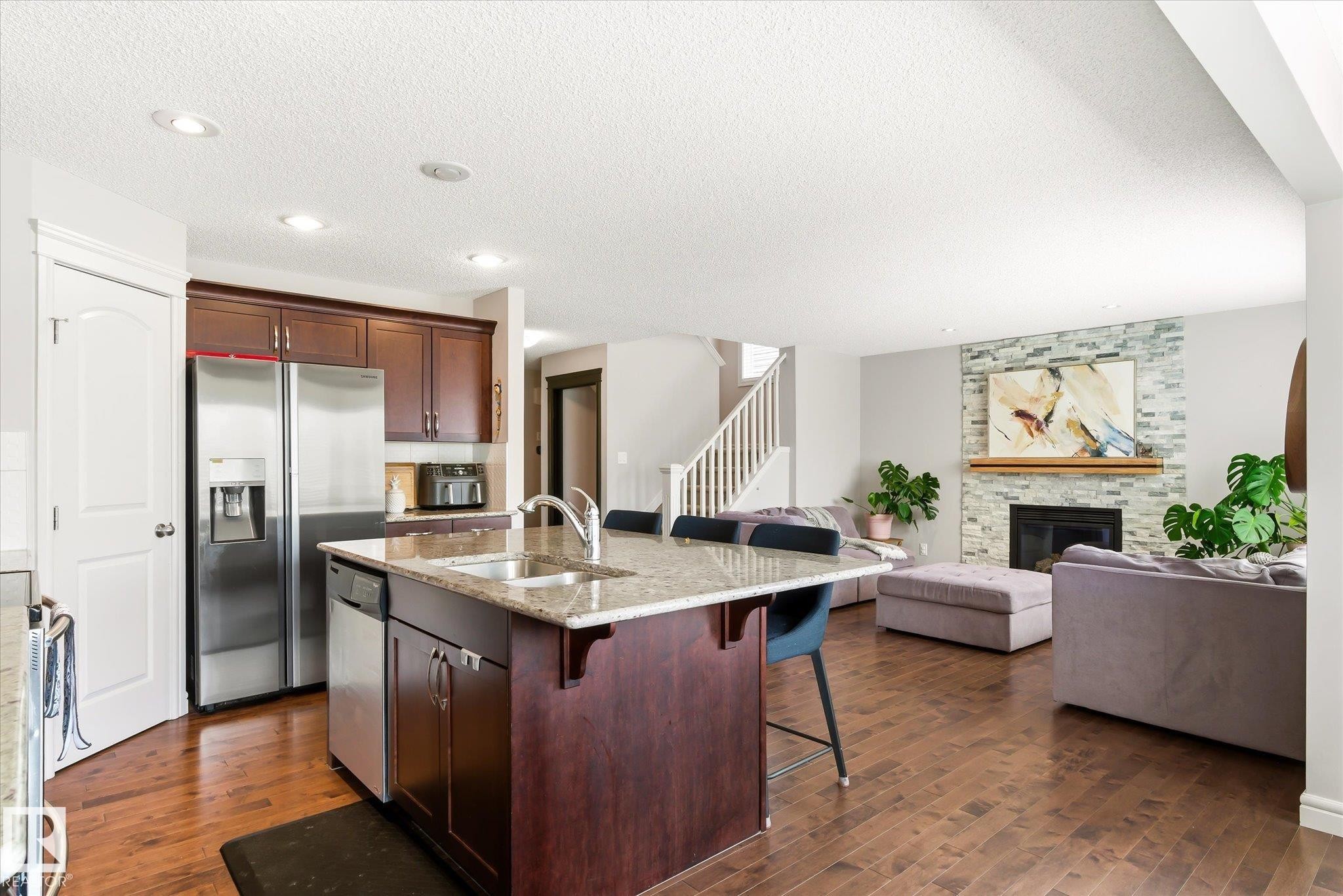 Open-concept kitchen featuring an island with stone countertop and integrated sink, stainless steel appliances, and rich wood-finish cabinetry - 3685 Westcliff Way, Edmonton, AB