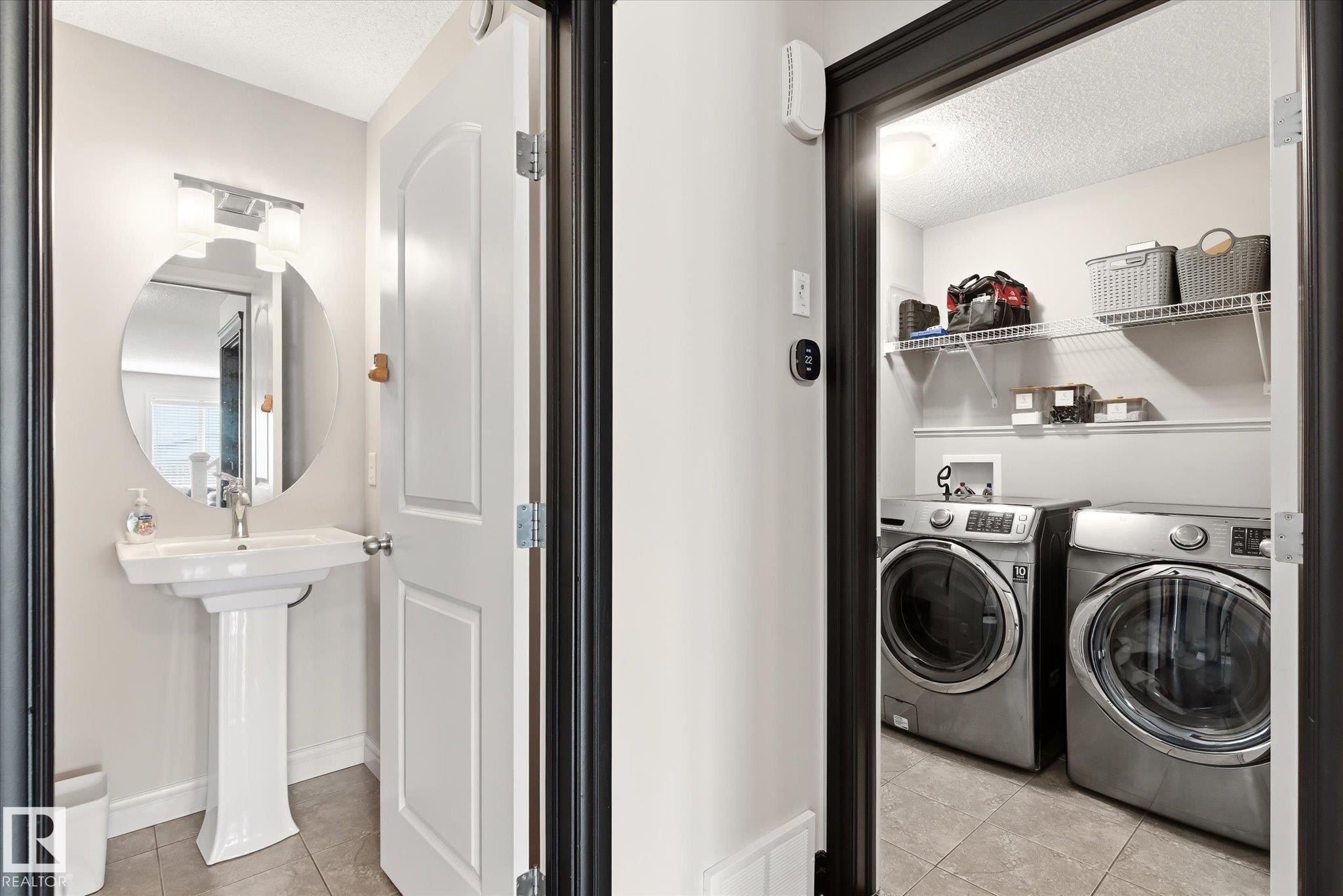 Pedestal sink with an oval mirror and vanity lighting, complemented by an adjacent laundry area featuring wire shelving - 3685 Westcliff Way, Edmonton, AB