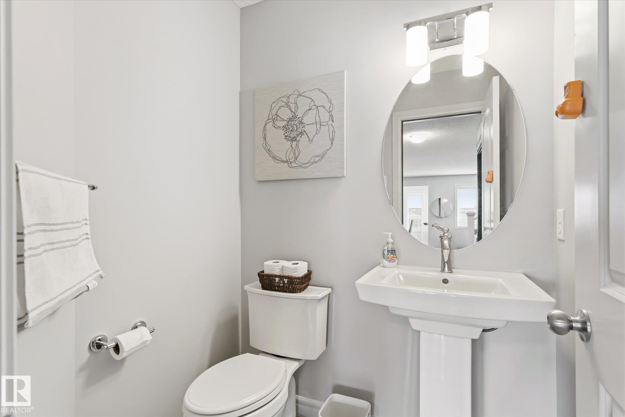 Pedestal sink with chrome faucet, circular mirror, and two-light vanity fixture - 3685 Westcliff Way, Edmonton, AB