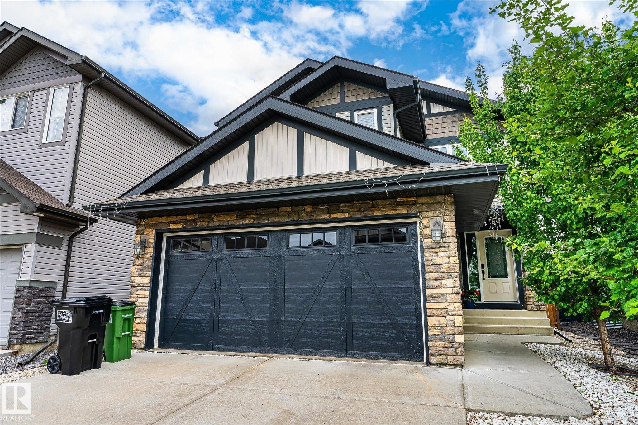 Exterior featuring stone veneer accents, multi-pane garage door, and a covered entry - 3685 Westcliff Way, Edmonton, AB