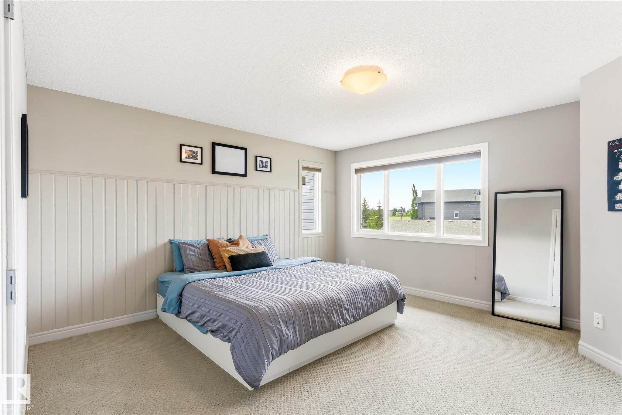 Bedroom featuring a large window, light-colored carpet flooring, a ceiling-mounted light fixture, and vertical paneling on one wall - 3685 Westcliff Way, Edmonton, AB