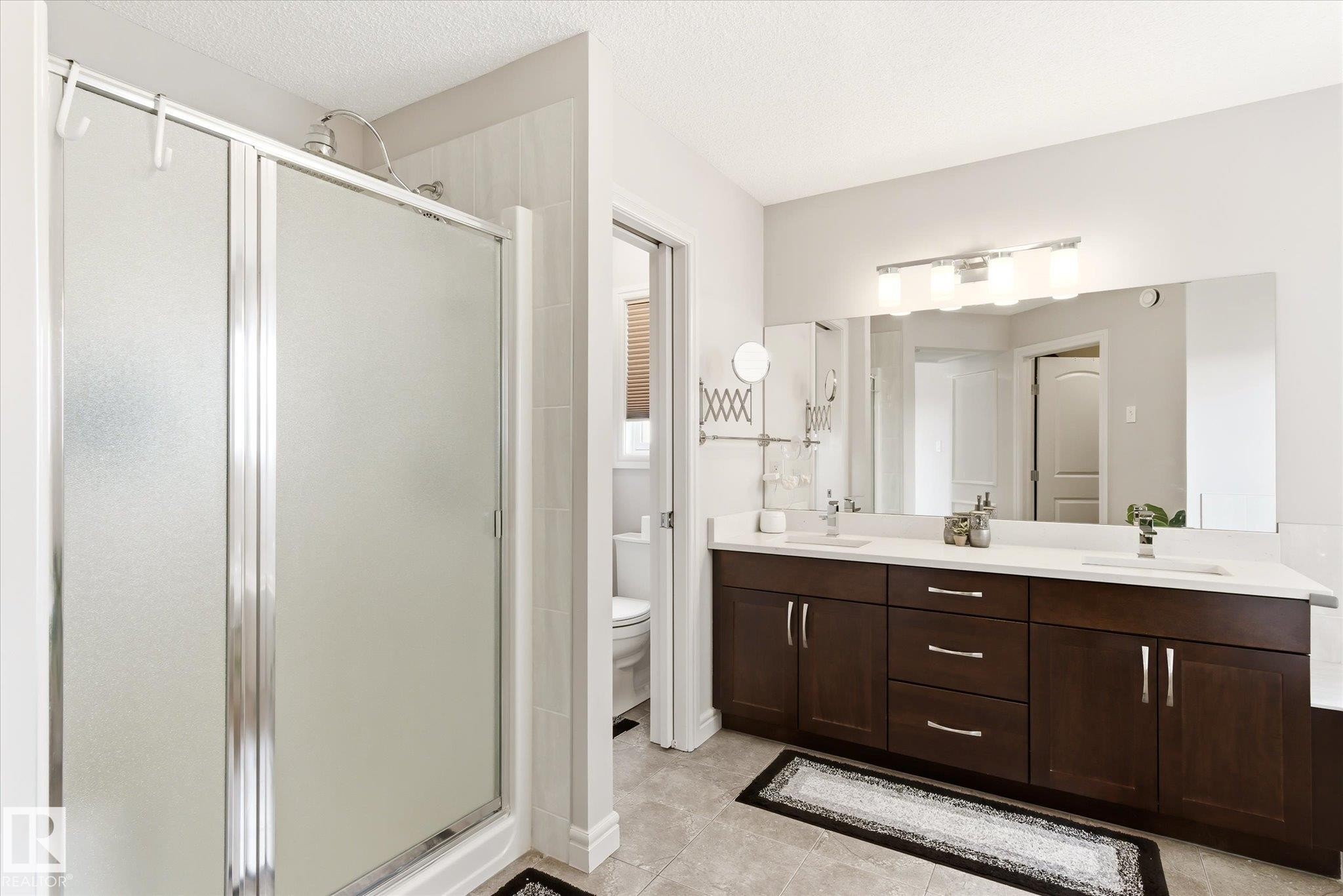 Full bathroom featuring a glass-enclosed shower, a dual-sink vanity with dark wood-finish cabinetry, a large vanity mirror, and overhead lighting - 3685 Westcliff Way, Edmonton, AB