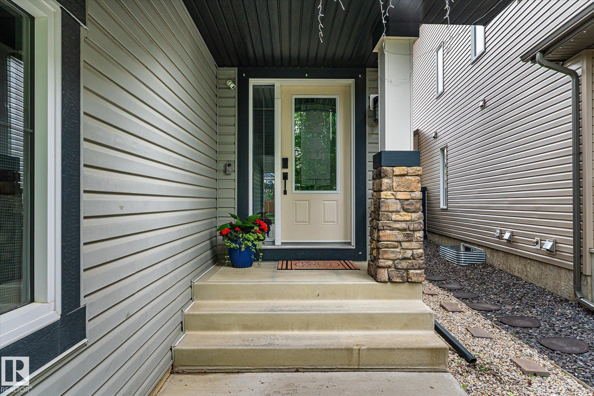 Inviting front entrance featuring a cream-colored main door with decorative glass, flanked by a stone-clad pillar and light-toned siding - 3685 Westcliff Way, Edmonton, AB