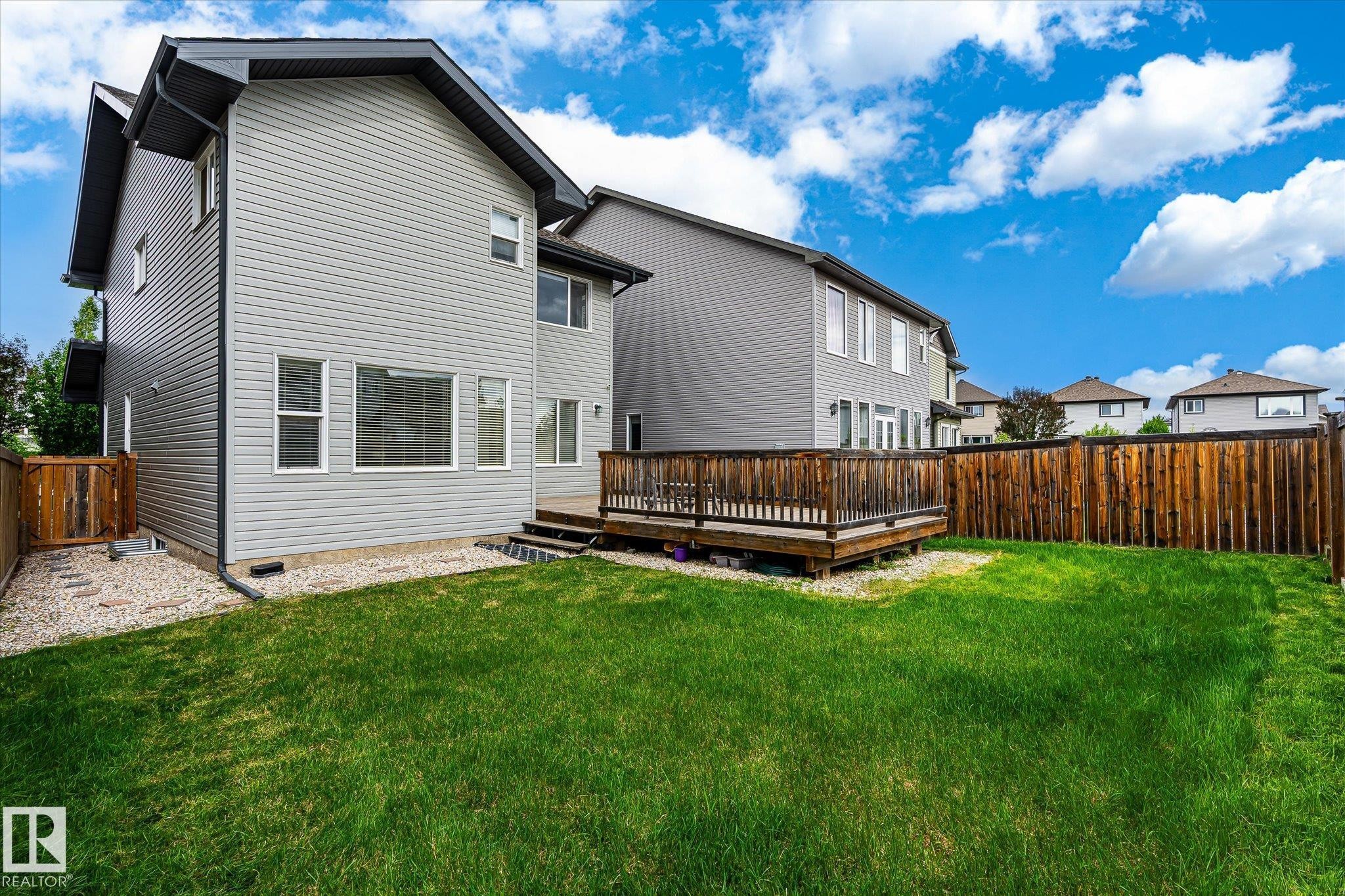 Expansive backyard featuring a manicured lawn, a large wooden deck with railing, and a tall privacy fence - 3685 Westcliff Way, Edmonton, AB