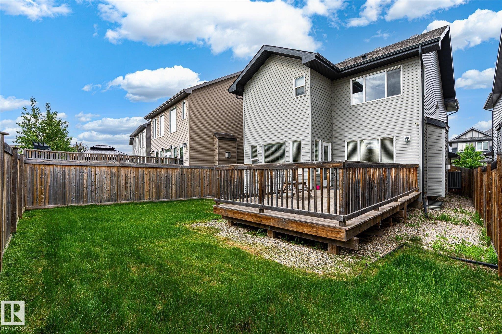 Private fenced backyard featuring a wooden deck, expansive lawn, and gravel landscaping - 3685 Westcliff Way, Edmonton, AB