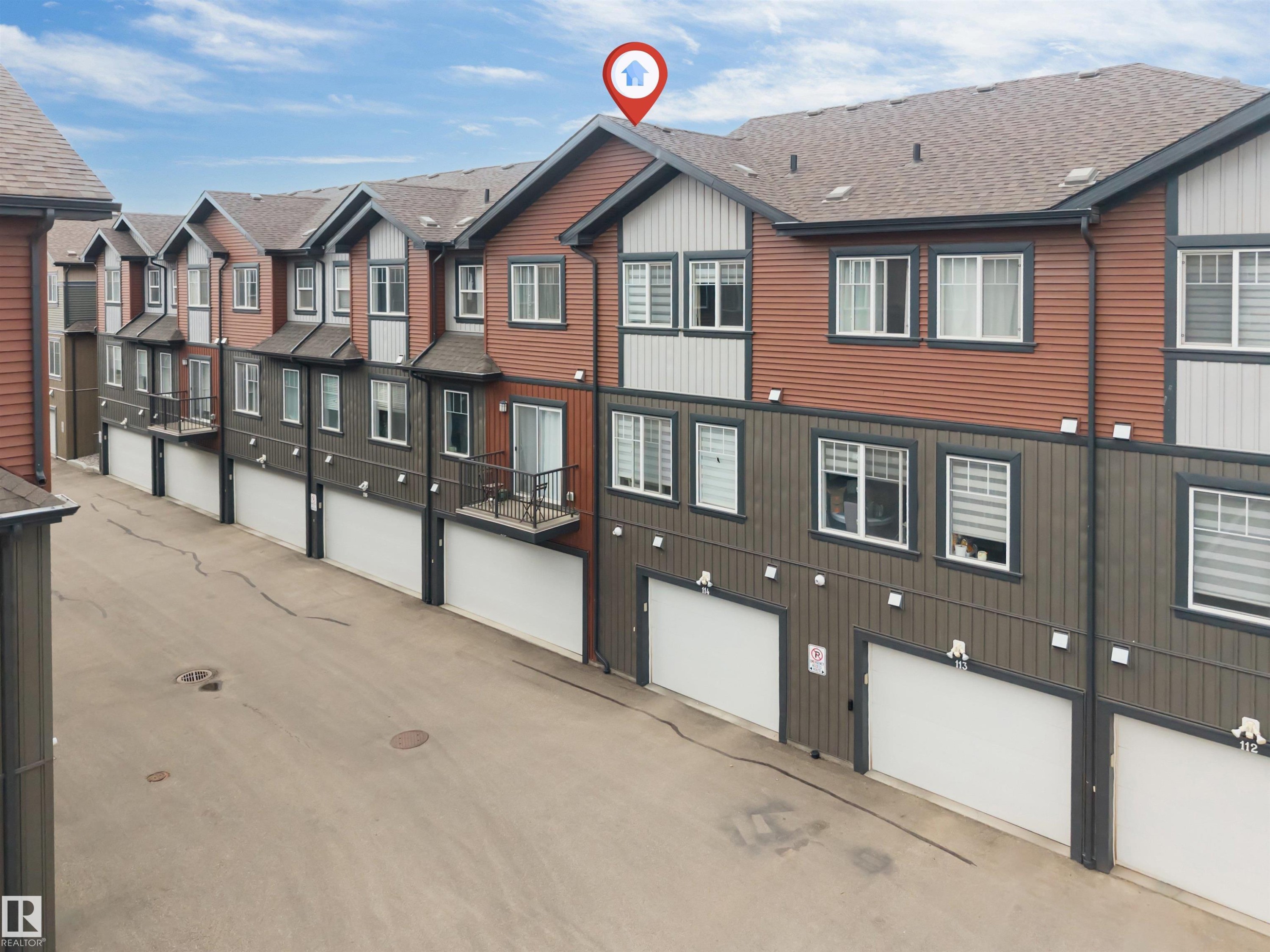 Multi-level townhome featuring a private balcony with black iron railings, a dedicated single-car garage, and a brown shingle roof - 116 3305 Orchards Link Sw, Edmonton, AB